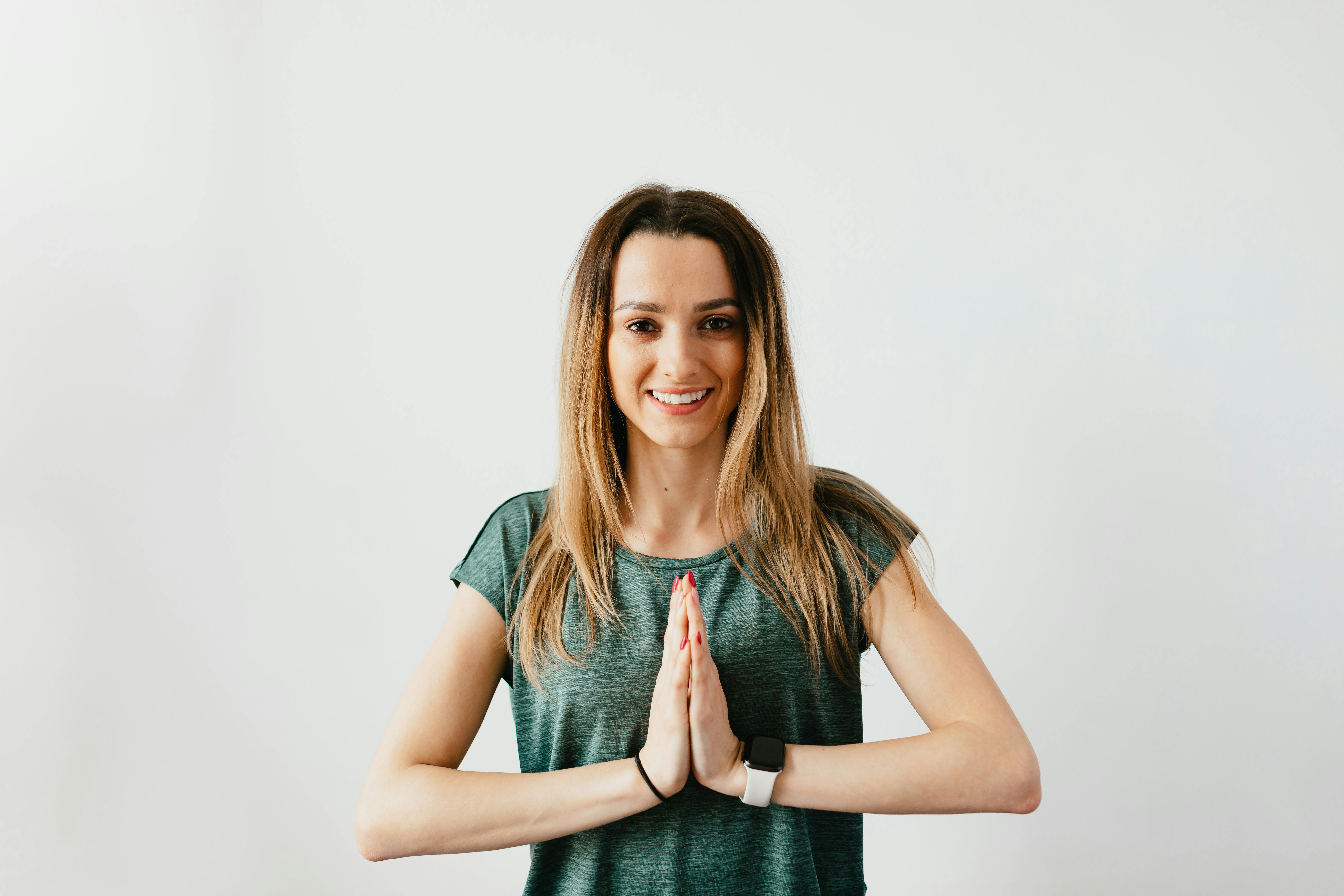 Glad blond woman in casual clothes and smart watch standing in Namaste pose while practicing yoga