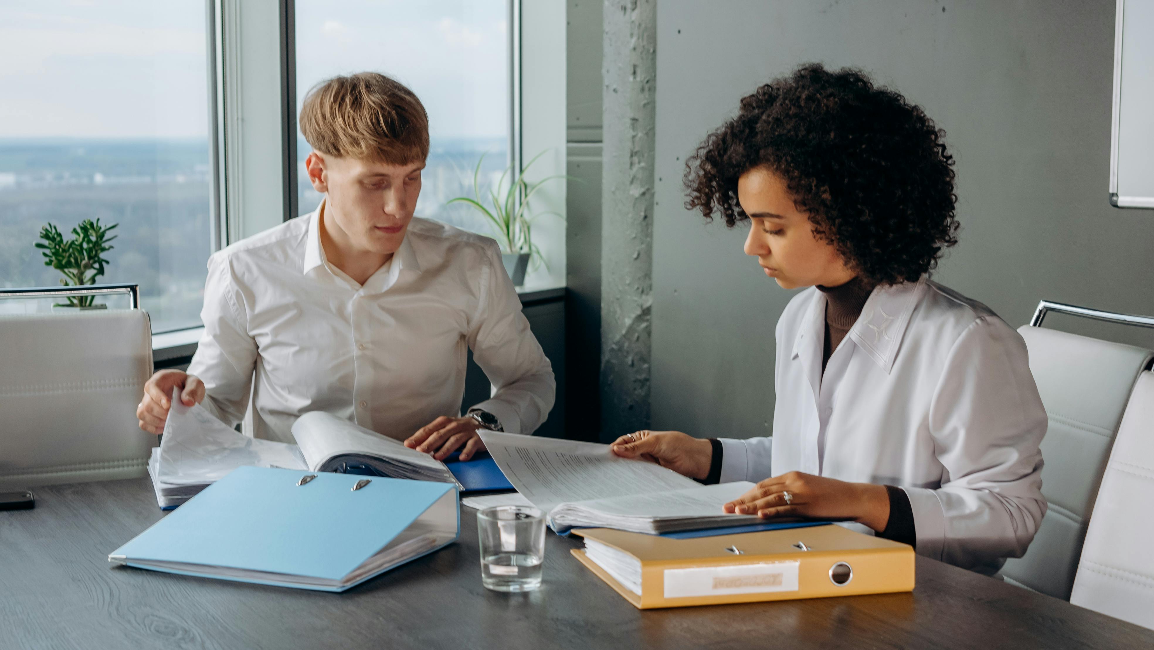 Colleagues in White Long Sleeve Shirts Sitting and Reading a Financial Report on a Conference Room