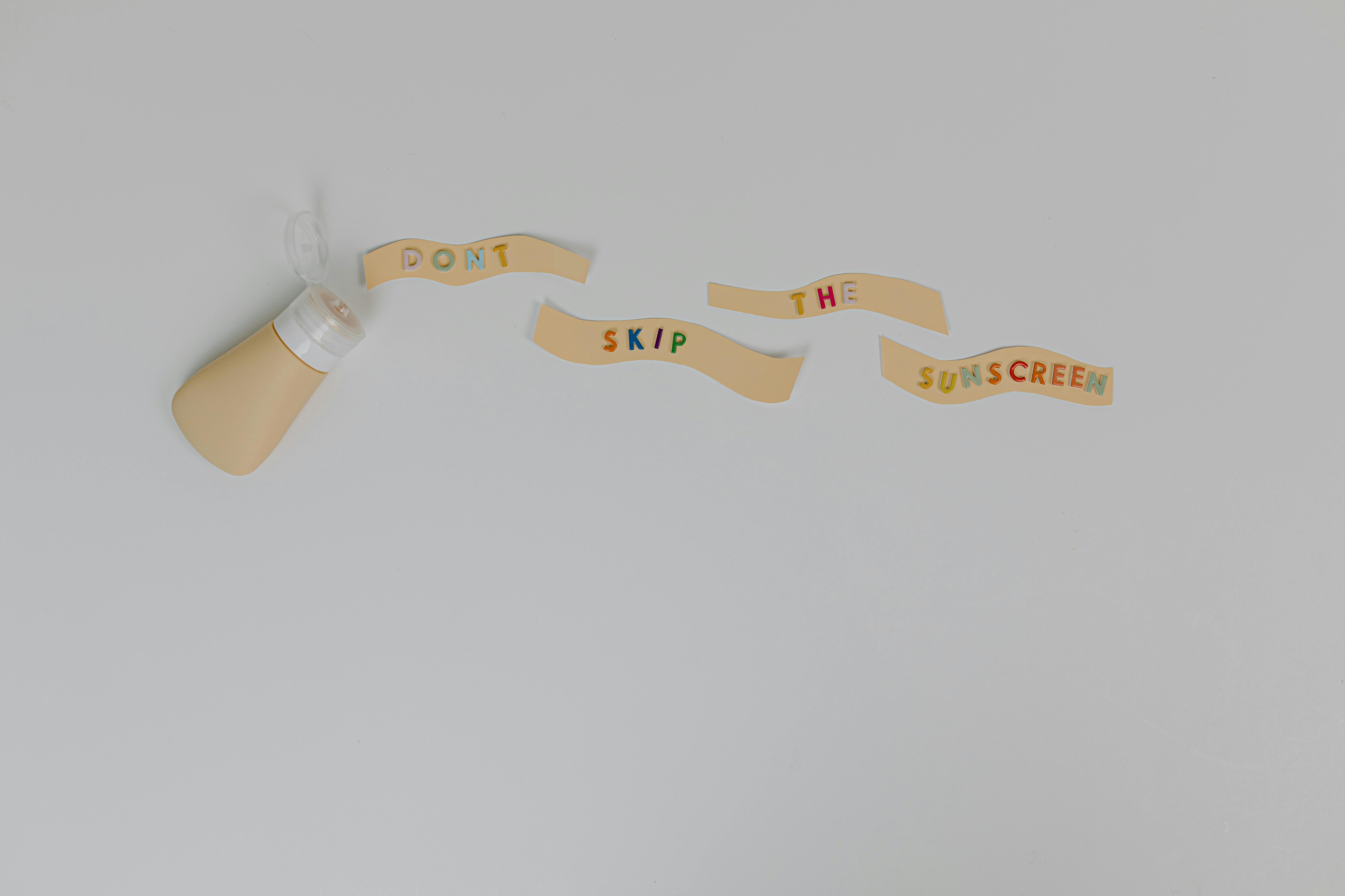 Text Saying "Don't Skin the Sunscreen" and a Bottle with Sunscreen Lying on White Background