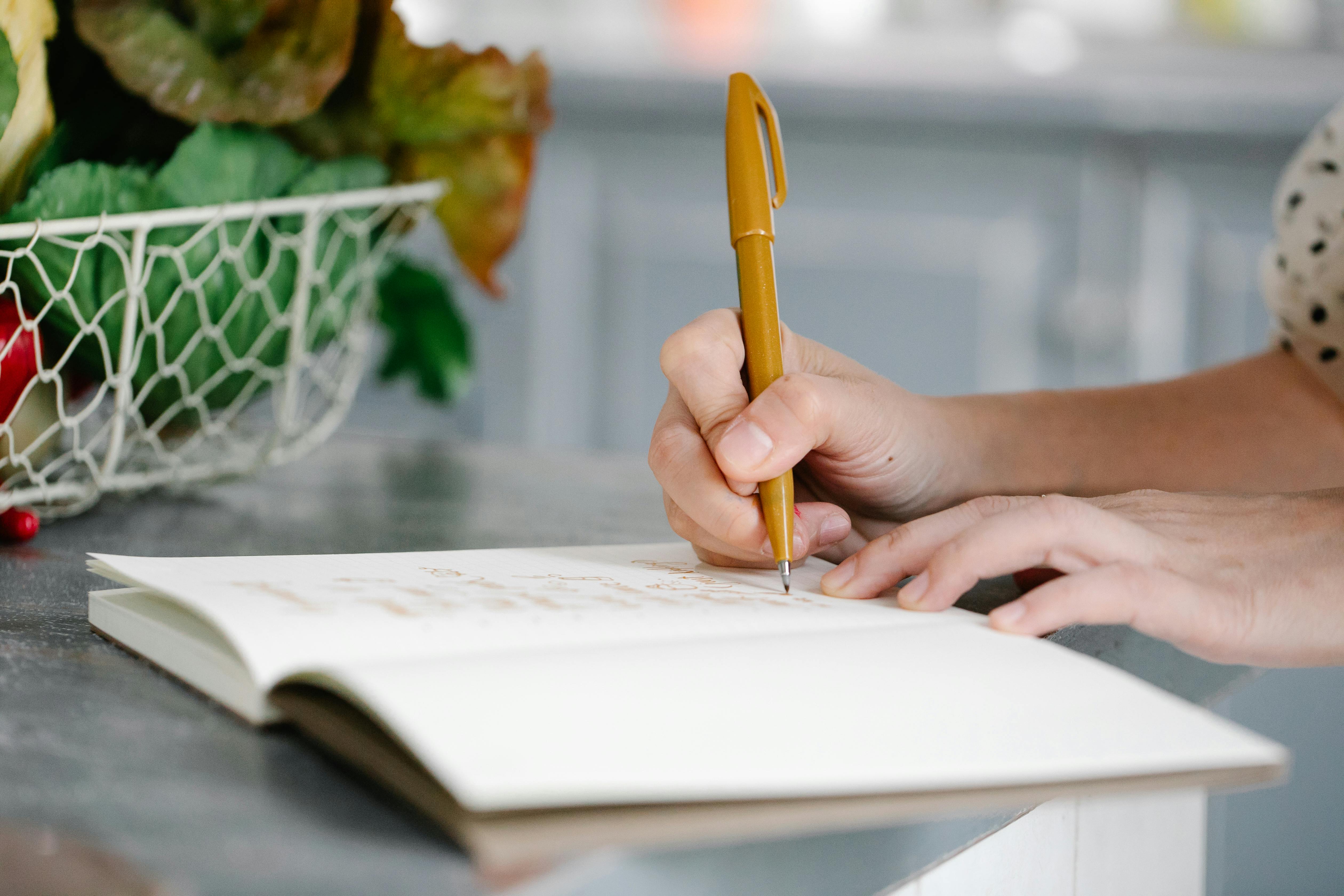 A Person Writing on a Notebook with a Brown Pen