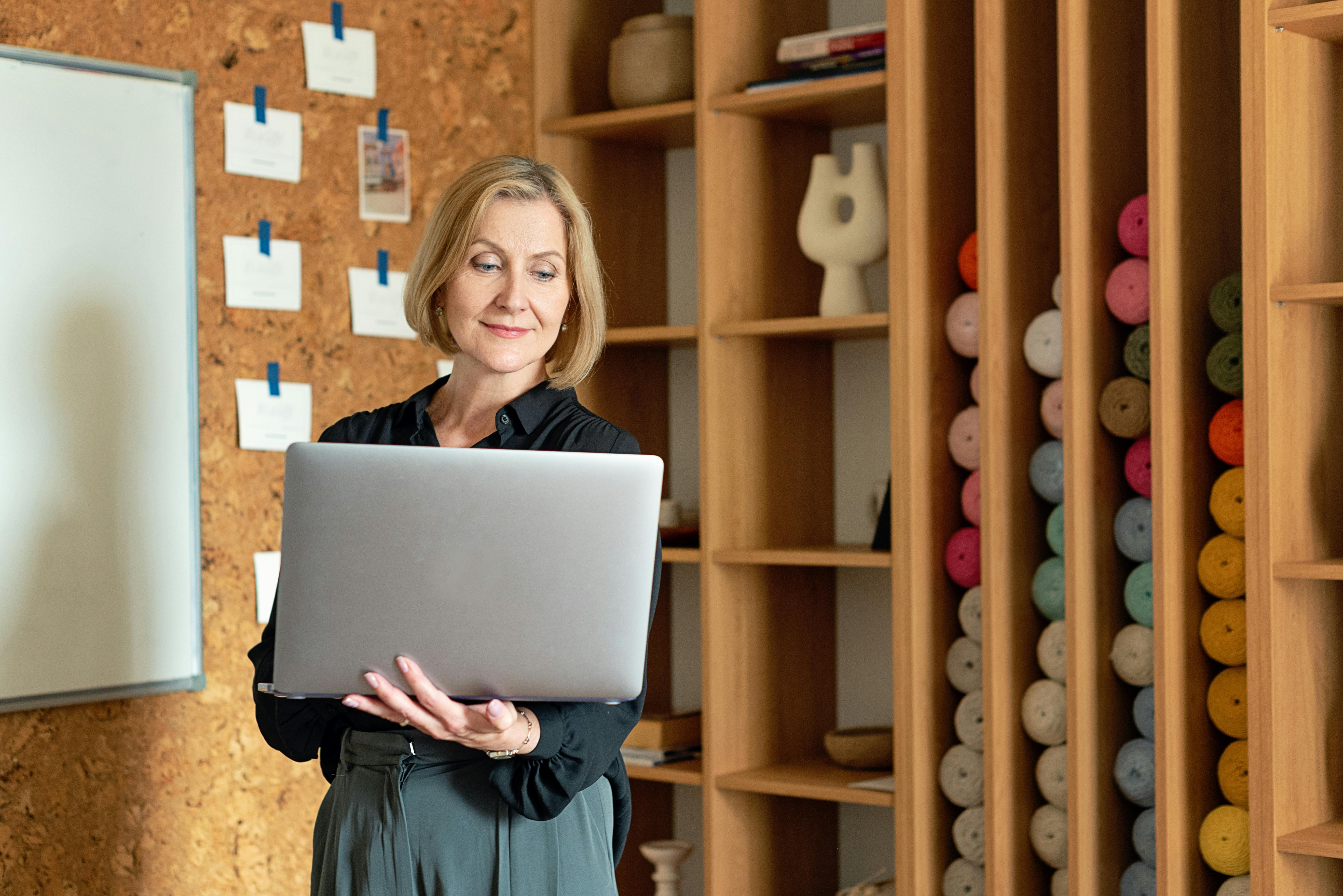 Smiling Woman in Black Long Sleeves Holding a Silver Laptop