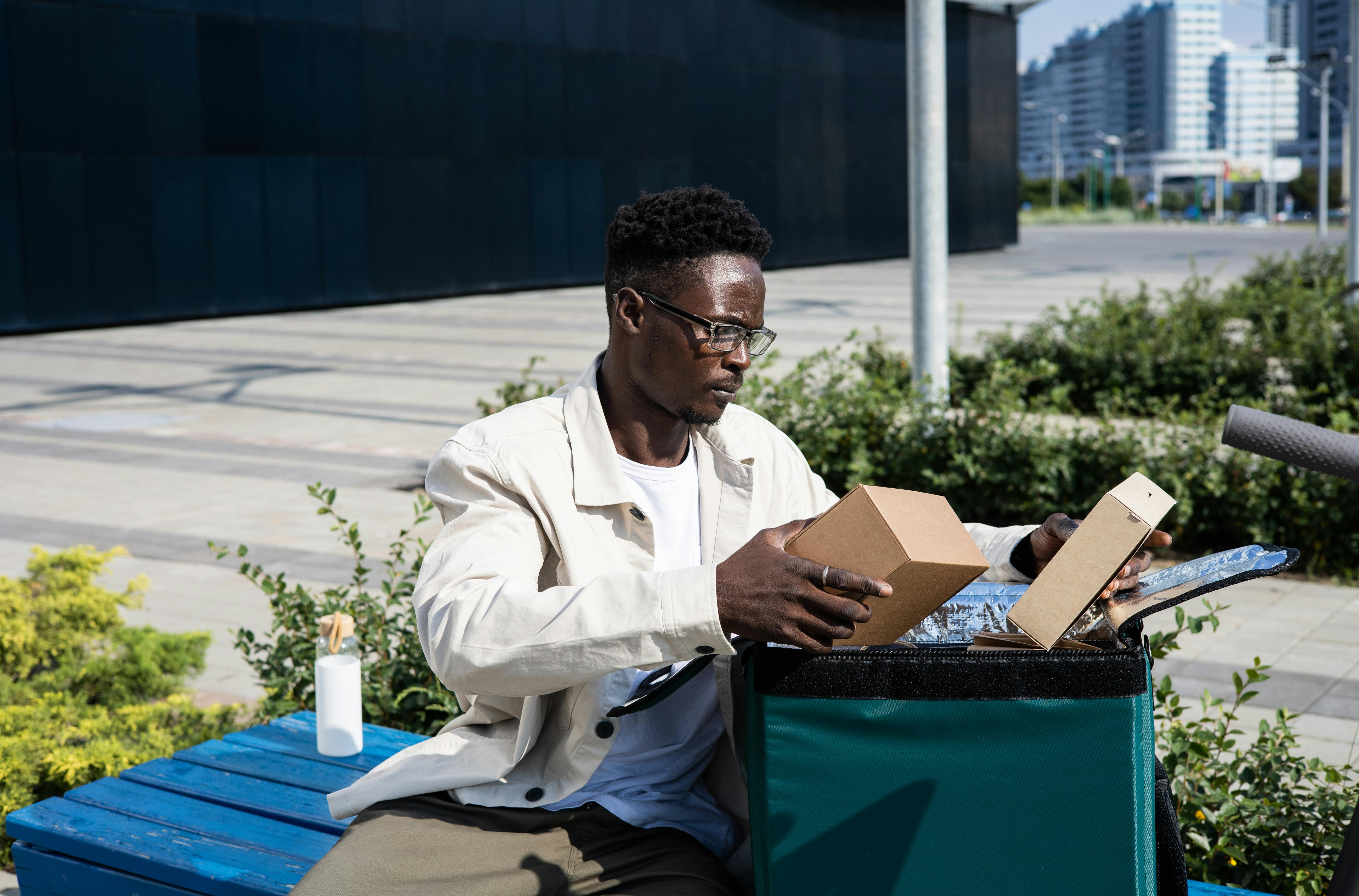 Man in White Dress Shirt Sitting on Blue Bench Looking at Parcels