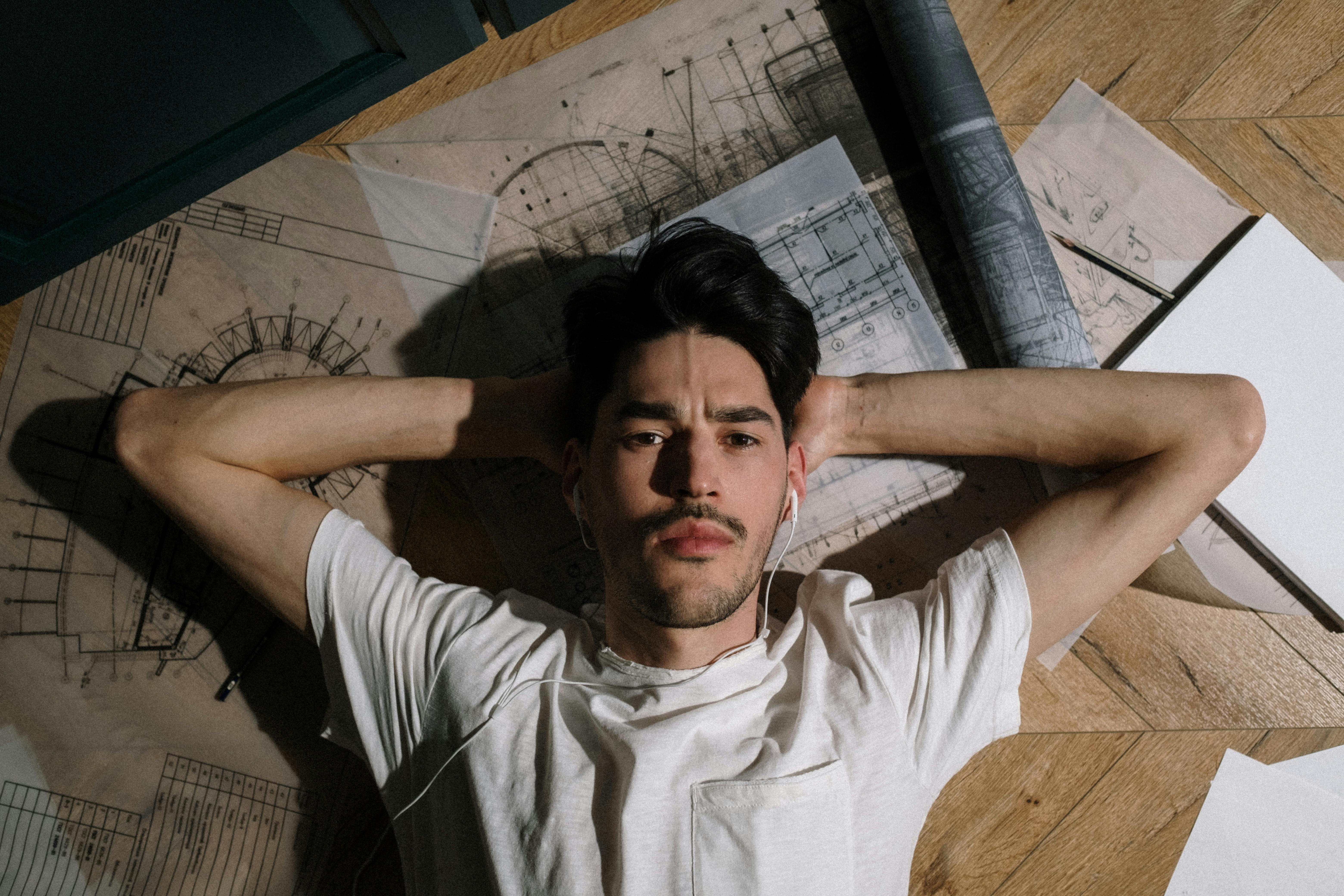 Adult man laying on floor among drawings with hands behind head