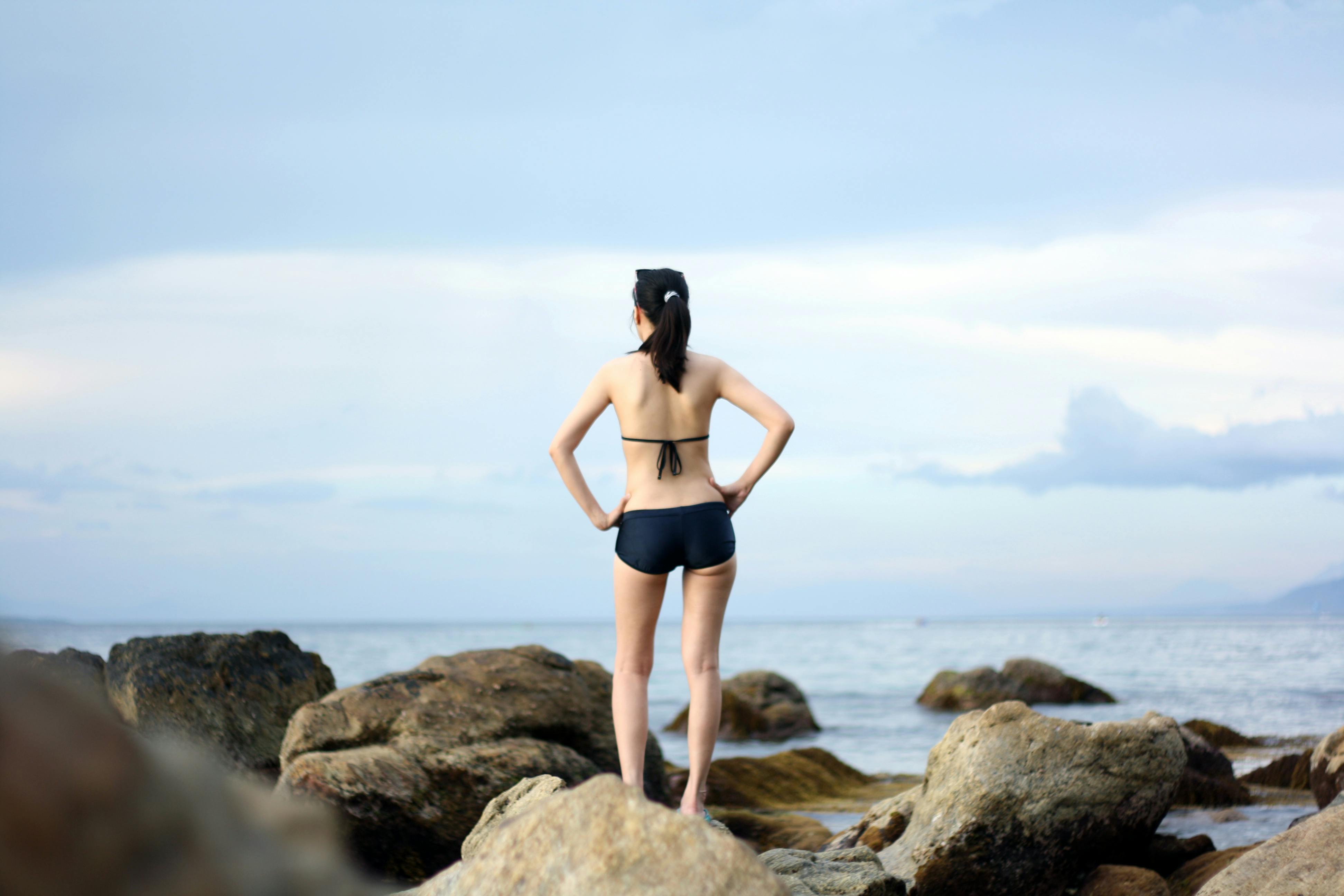 Woman Both Hand Akimbo Standing on Rock Facing Through Body of Water