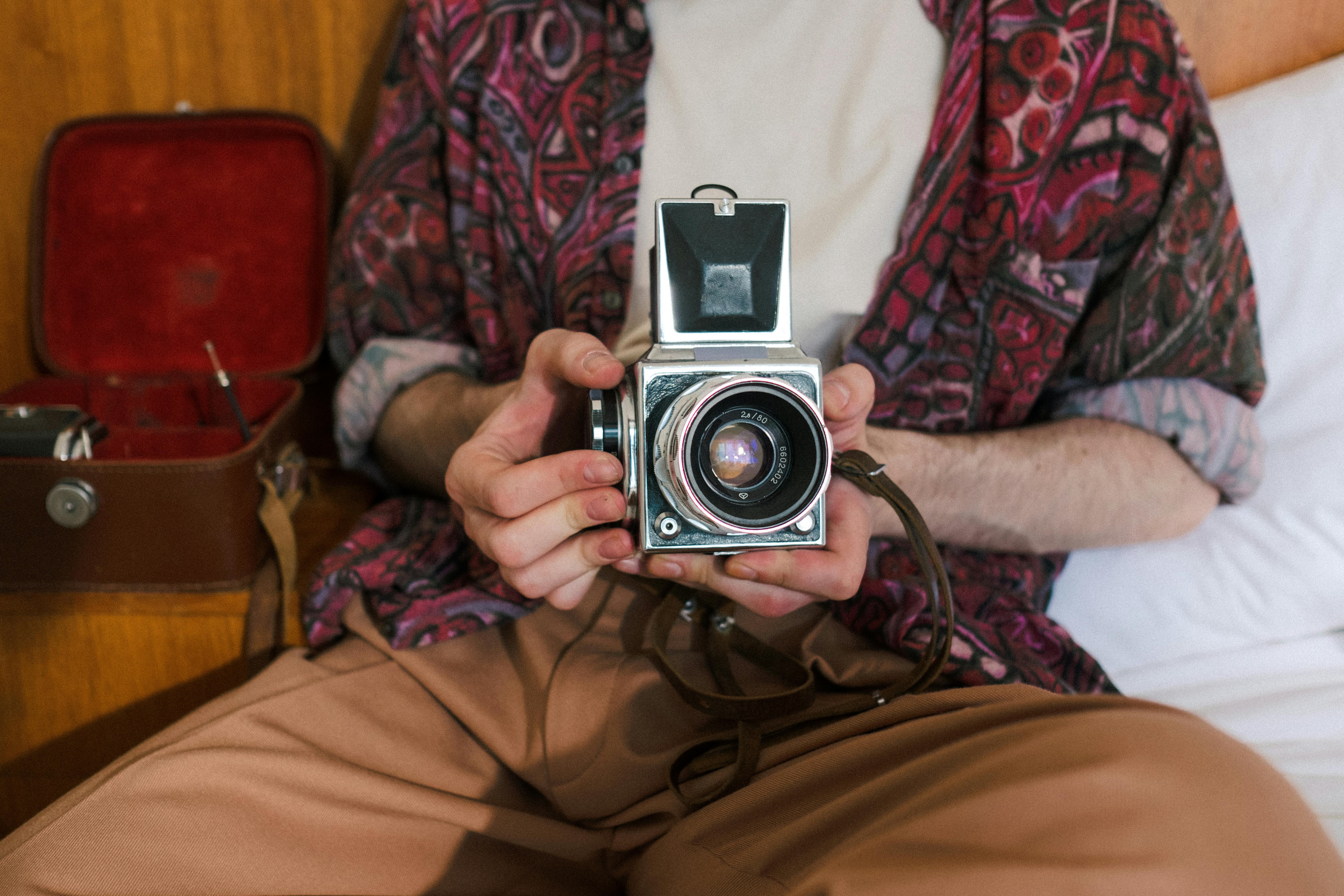 Unrecognizable Sitting Man Holding Analog Camera and Filming at Home