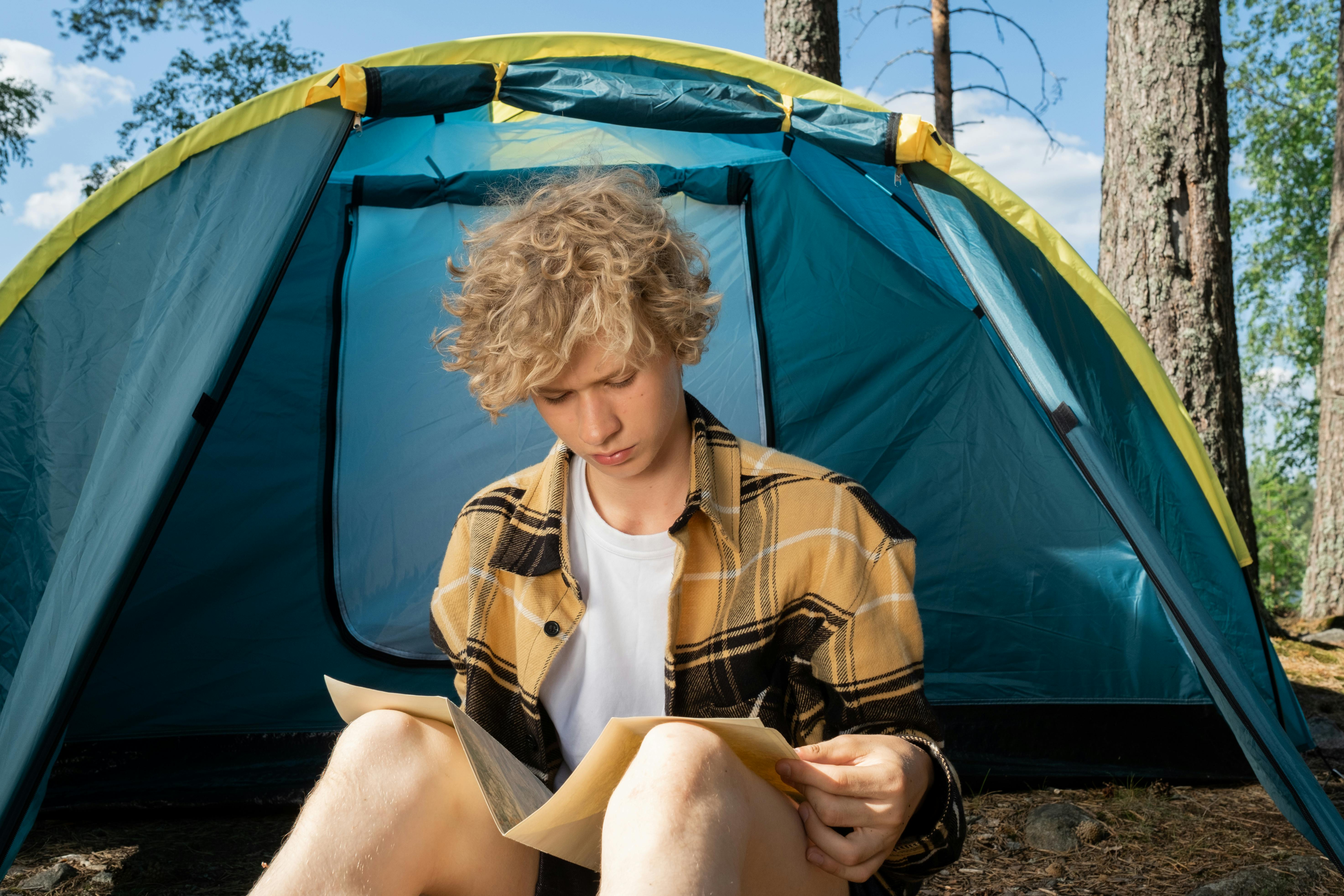 Tenager Sitting by Tent and Reading Map