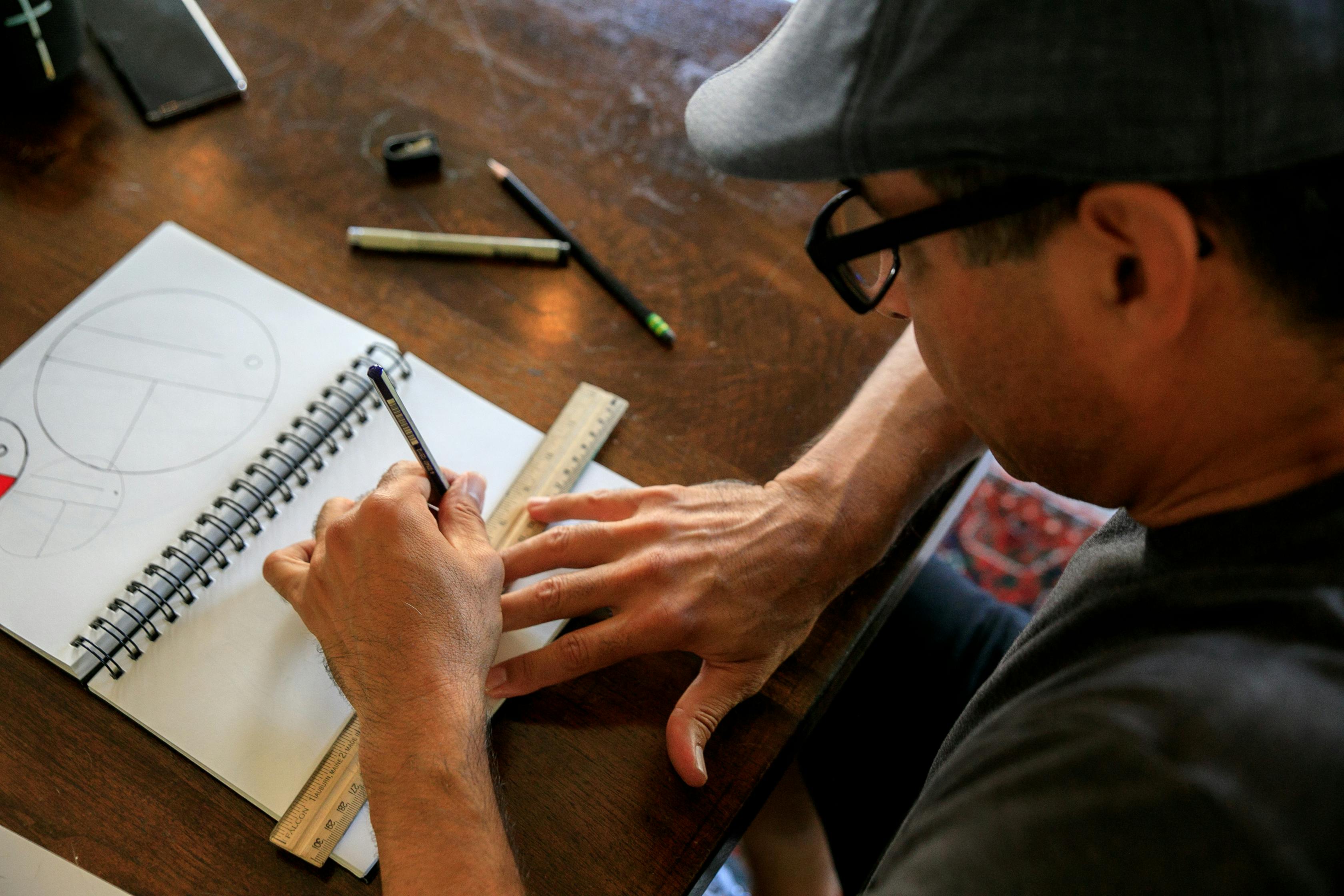 Man Sitting at the Table and Drawing in the Notebook