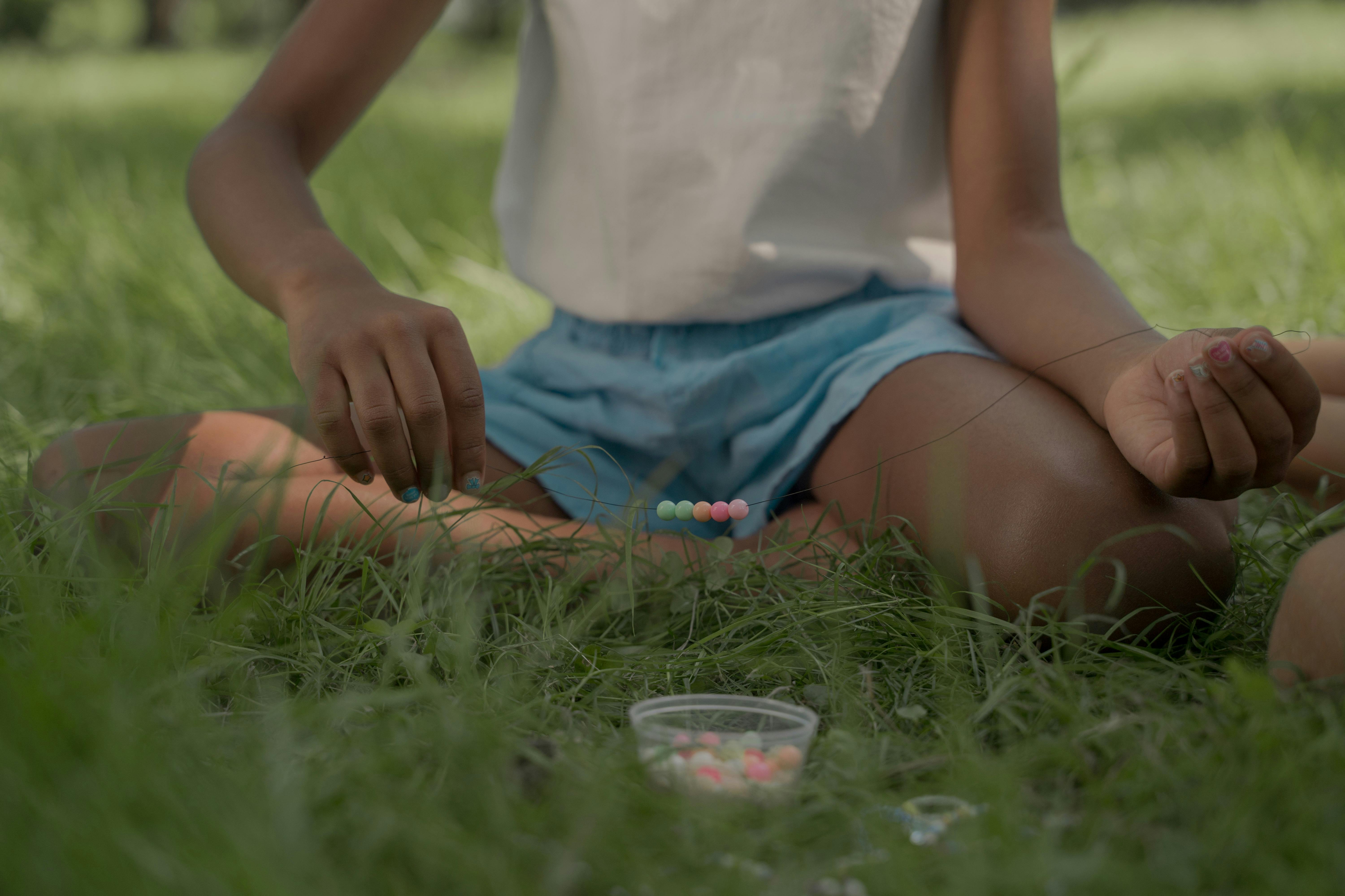 Girl Sitting on Grass Making Beads Necklace