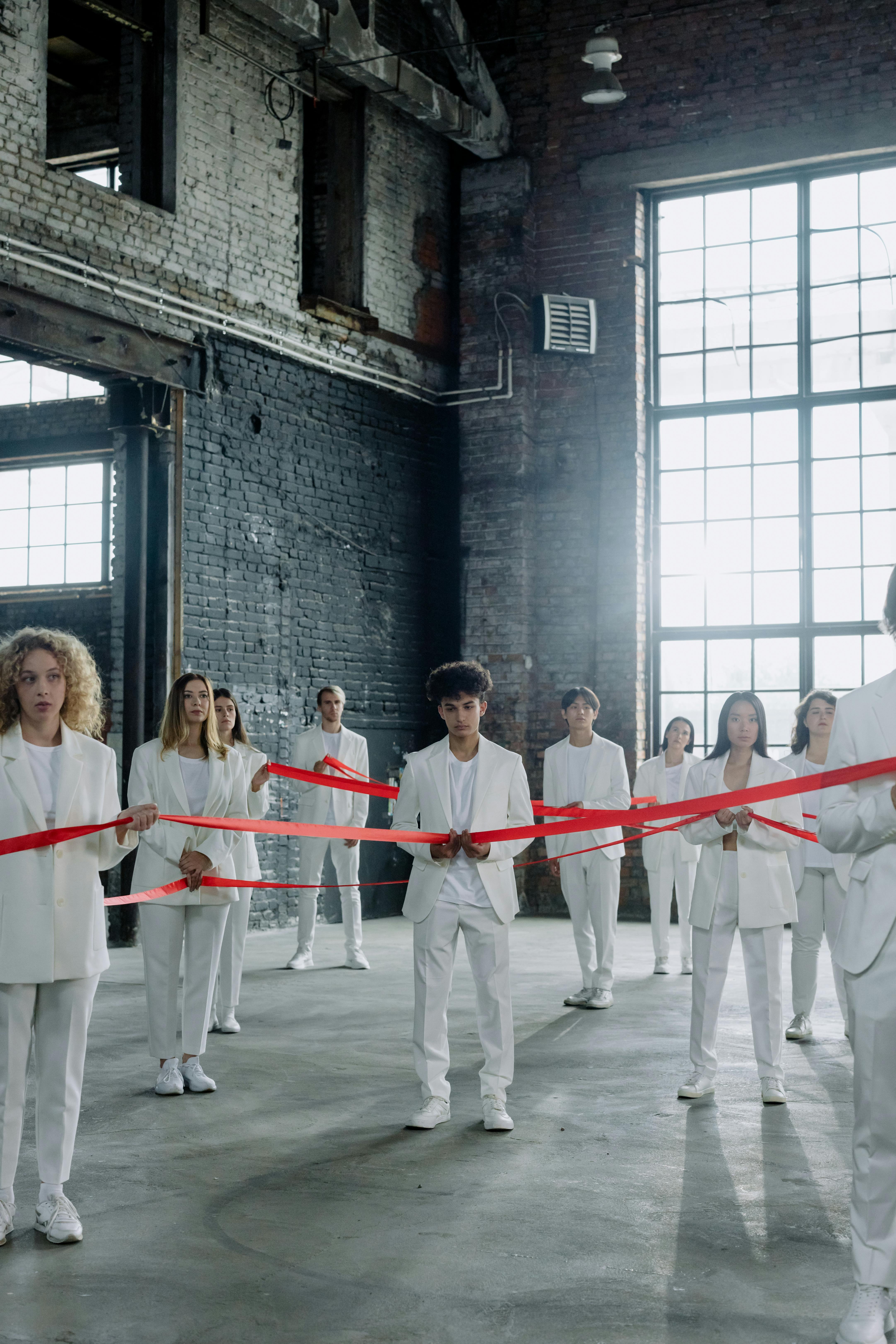 Group of People in White Clothes holding a Red Ribbon