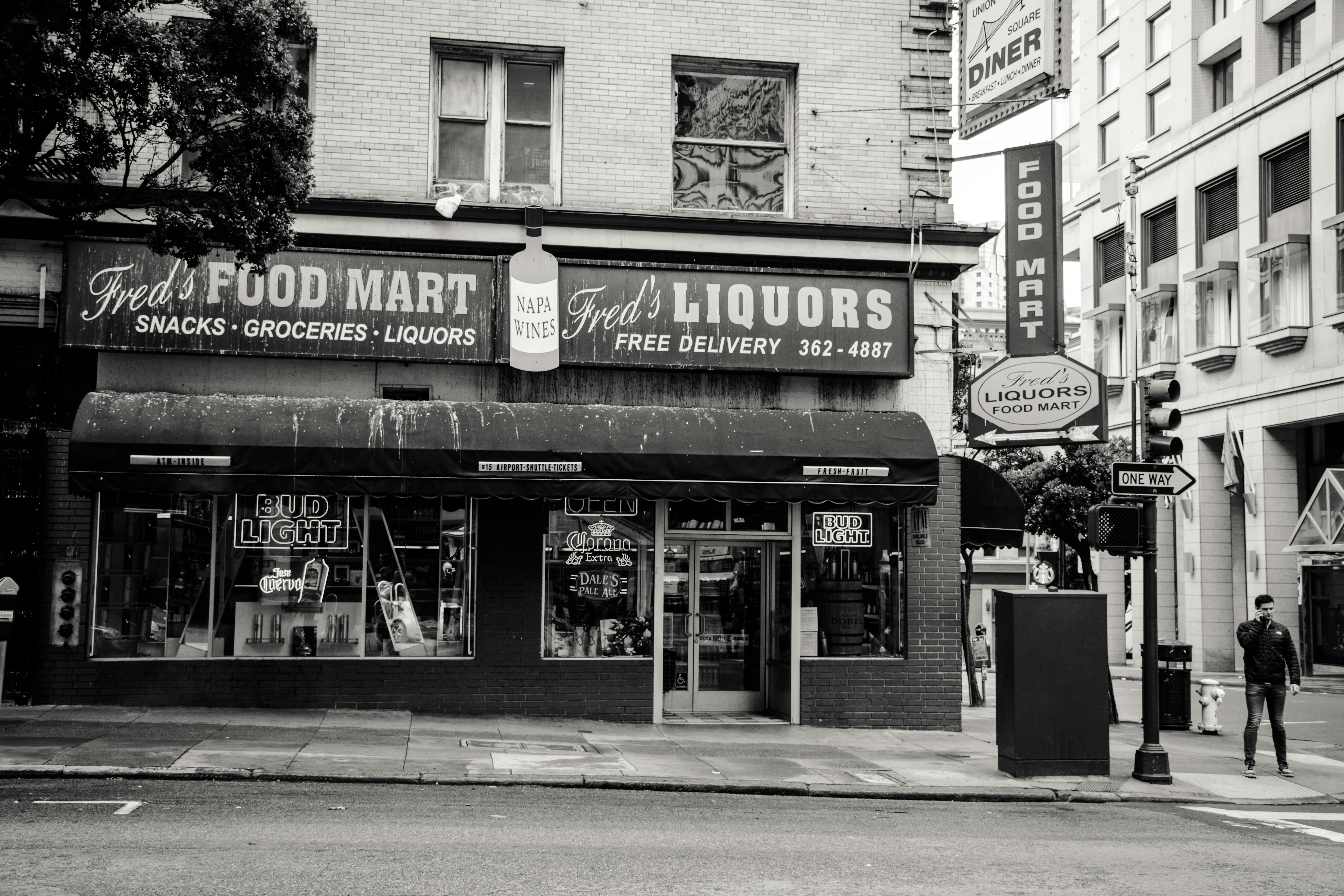 Greyscale Photo of Man Standing on Road Near Fred's Liqours Building