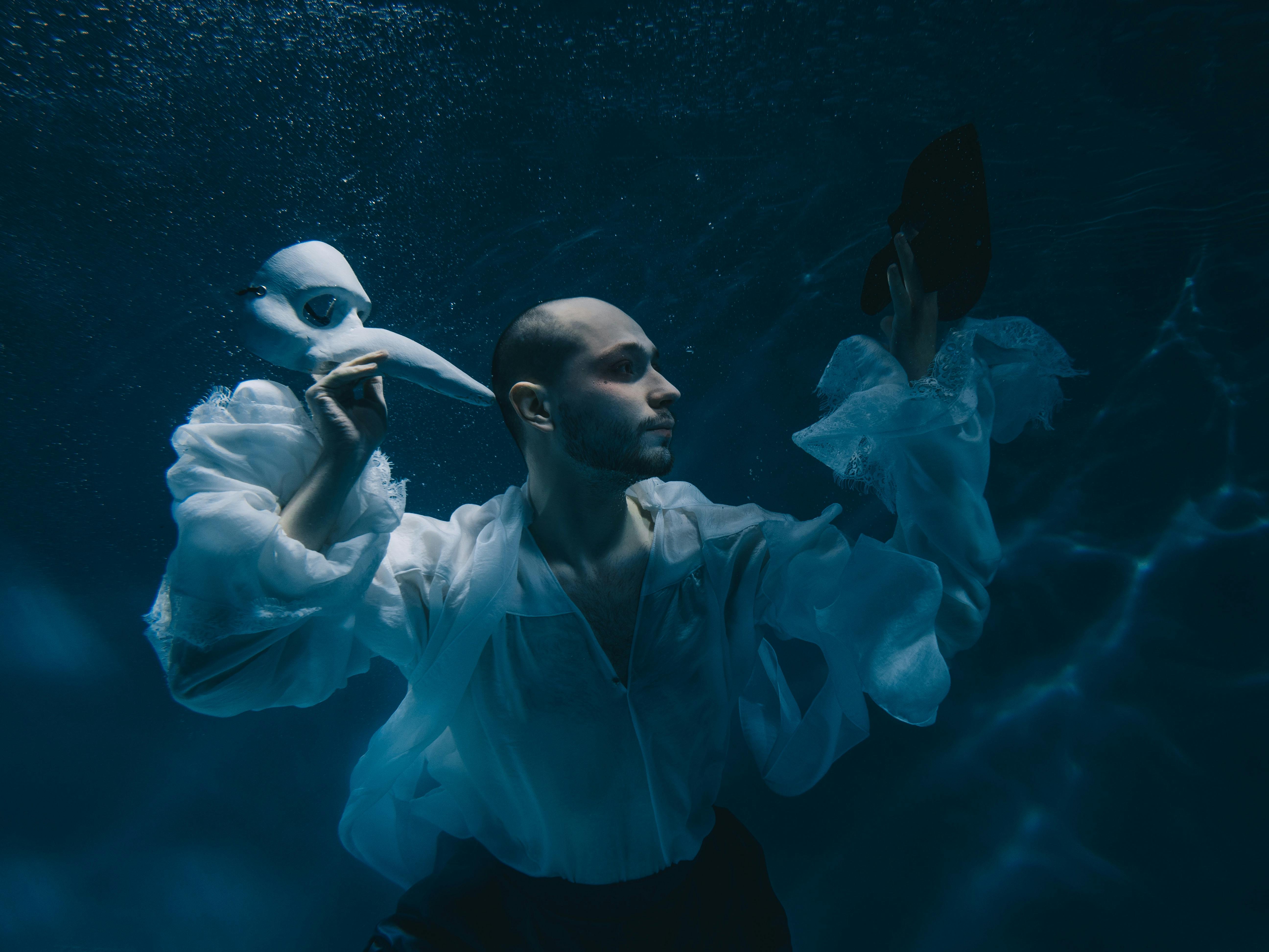 Man in Shirt Posing Underwater and Holding Theatre Mask