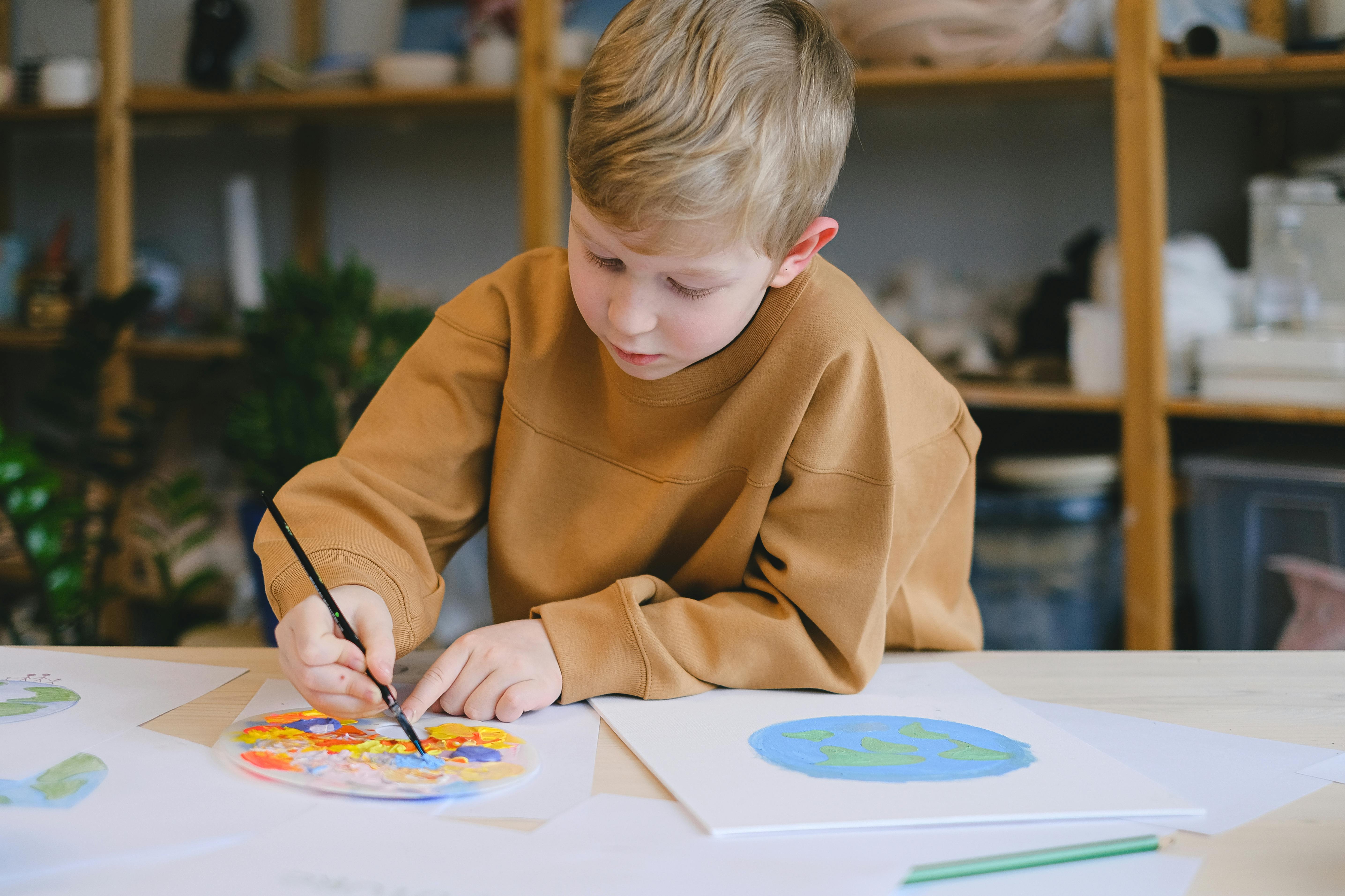 A Boy in Brown Long Sleeves Sweatshirt Painted  a Globe on White Paper