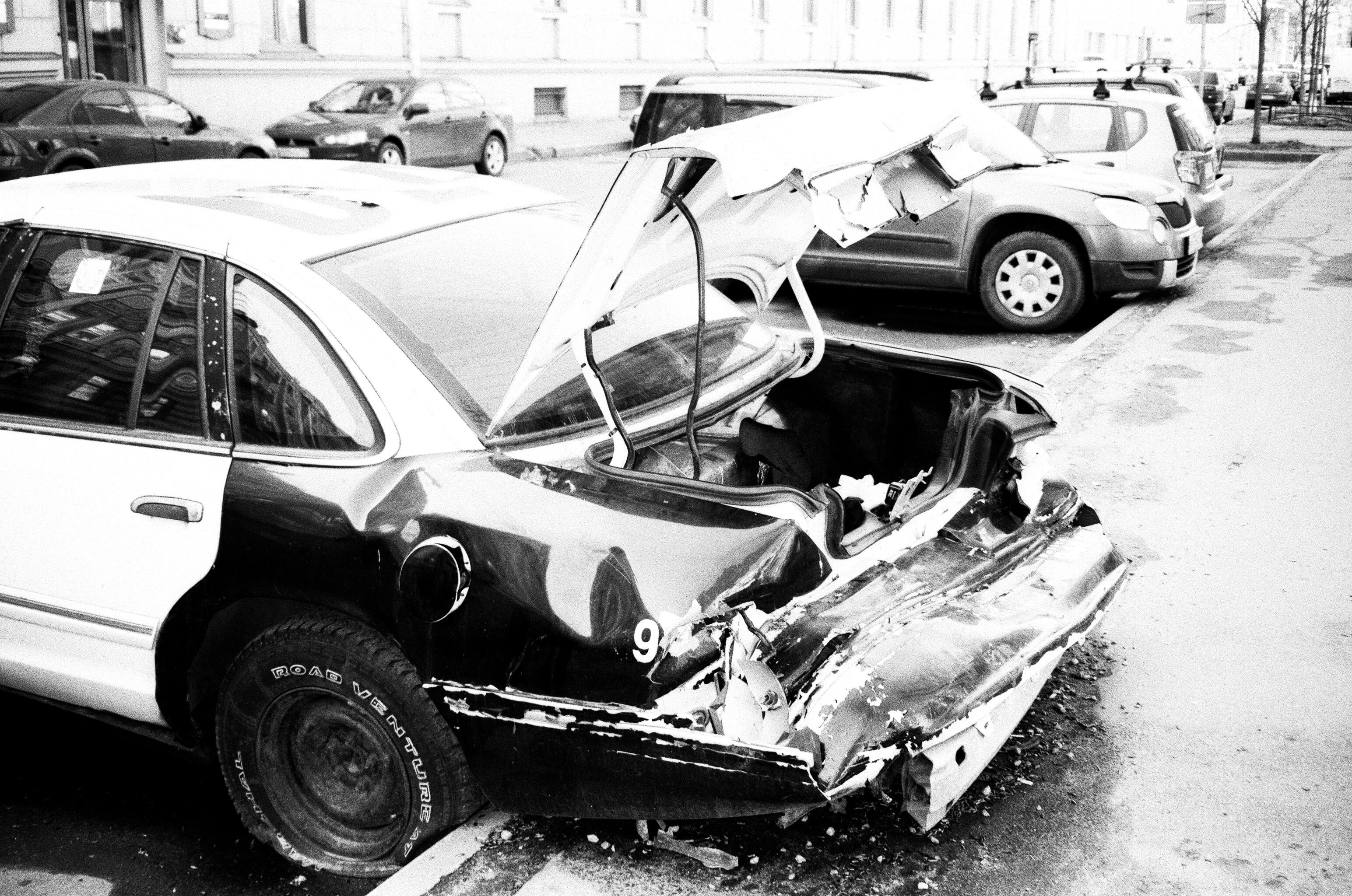 Grayscale Photo of Wrecked Car Parked Outside