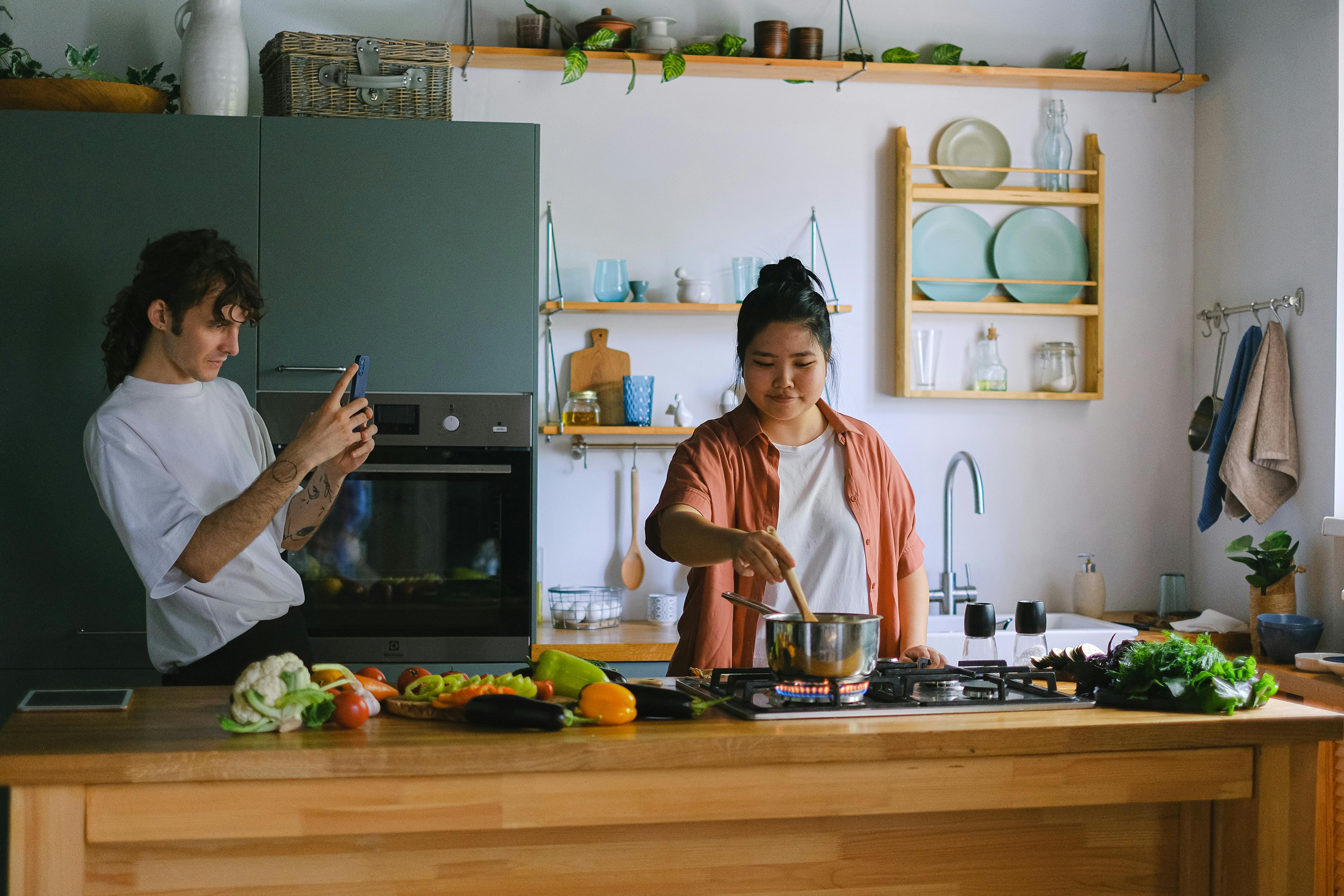 Man Taking a Picture of a Woman Cooking in a Kitchen