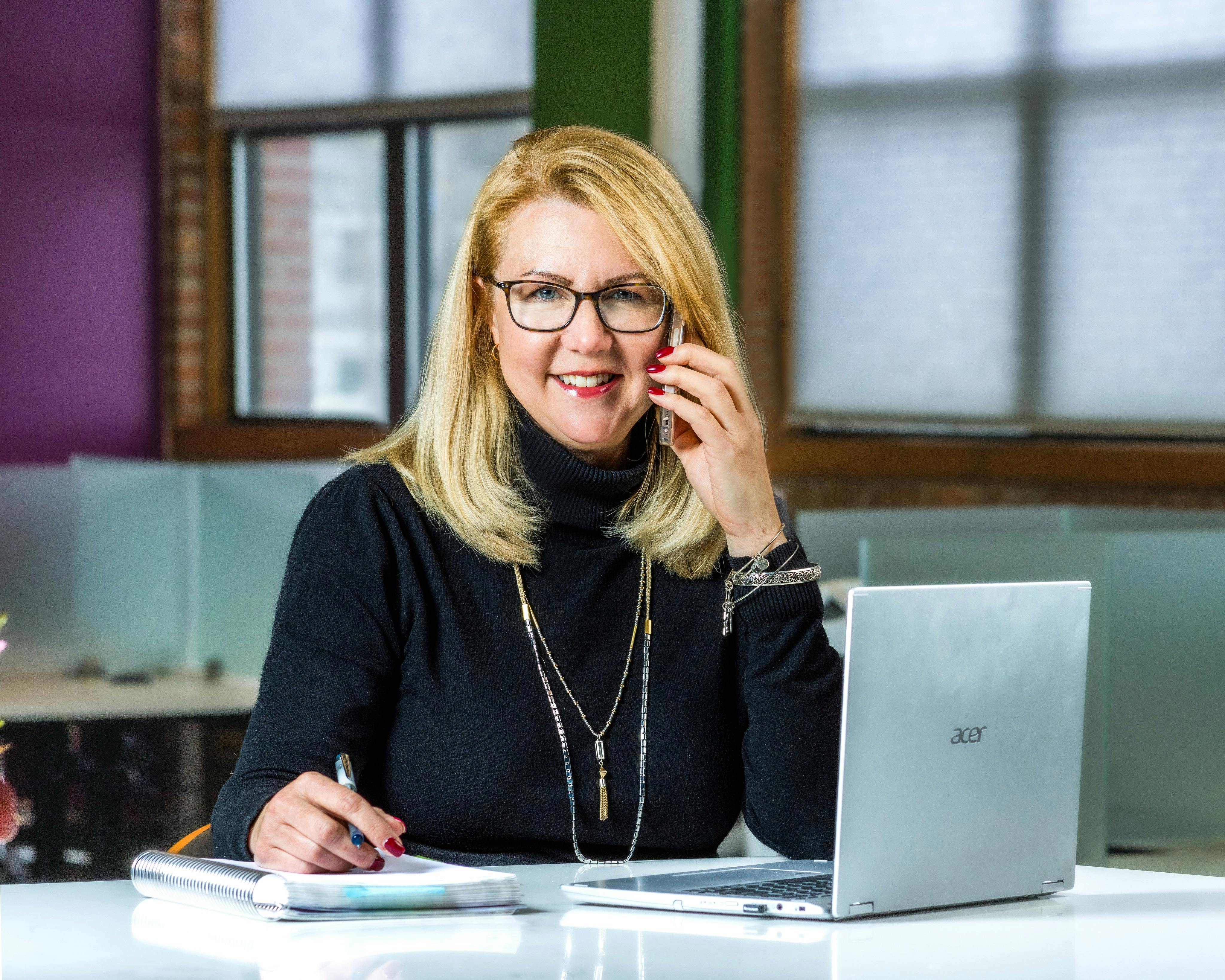 Woman at the Desk Using a Laptop and Phone