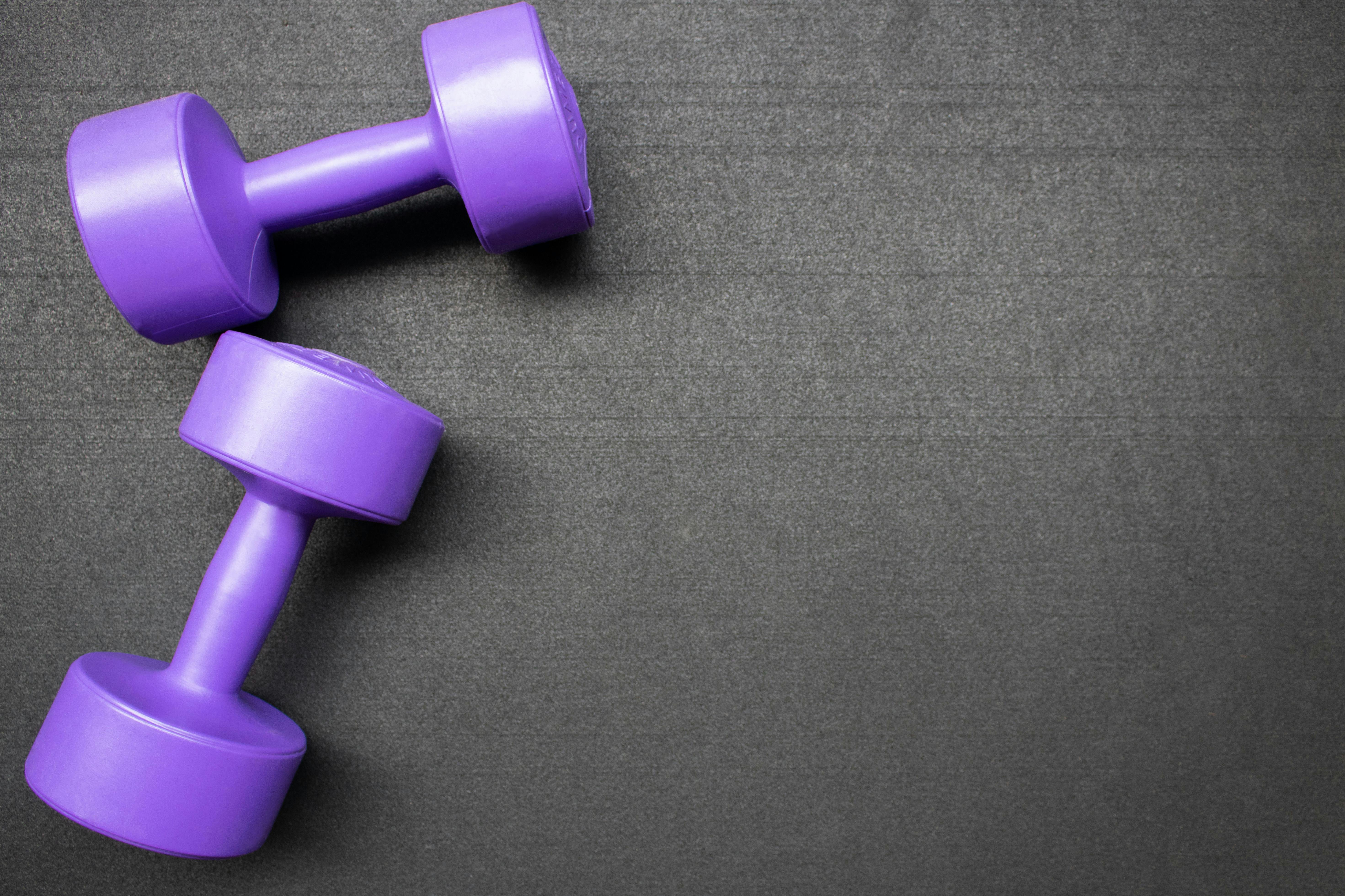 Set of two purple dumbbells on the floor at the gym. Top down view flat lay with fitness equipment on a black background. Left side alignment with empty space for text. Weight training con...