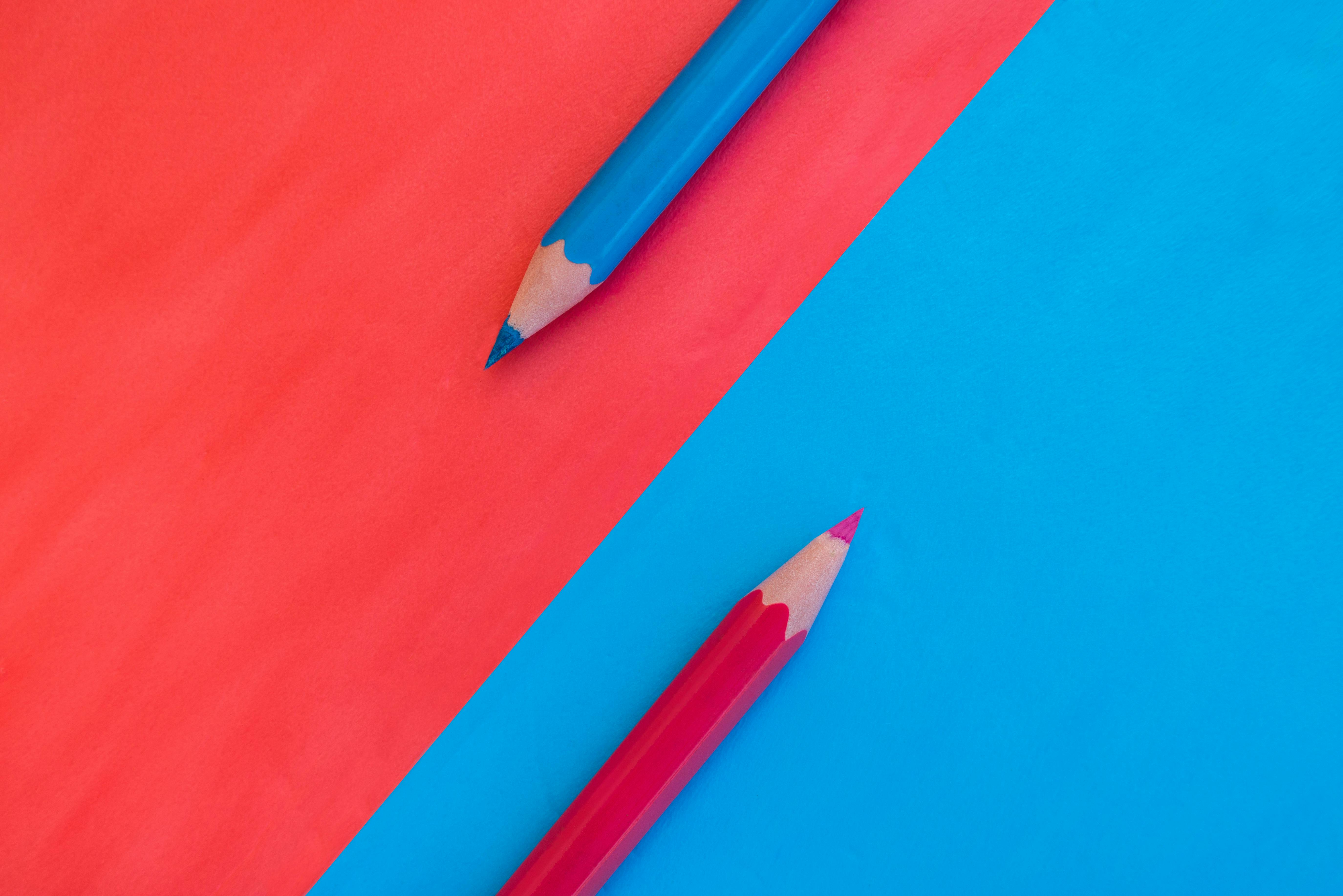 Pink and blue background divided diagonally with two matching colored pencils placed on opposite colors. Top down view flat lay with empty space for text