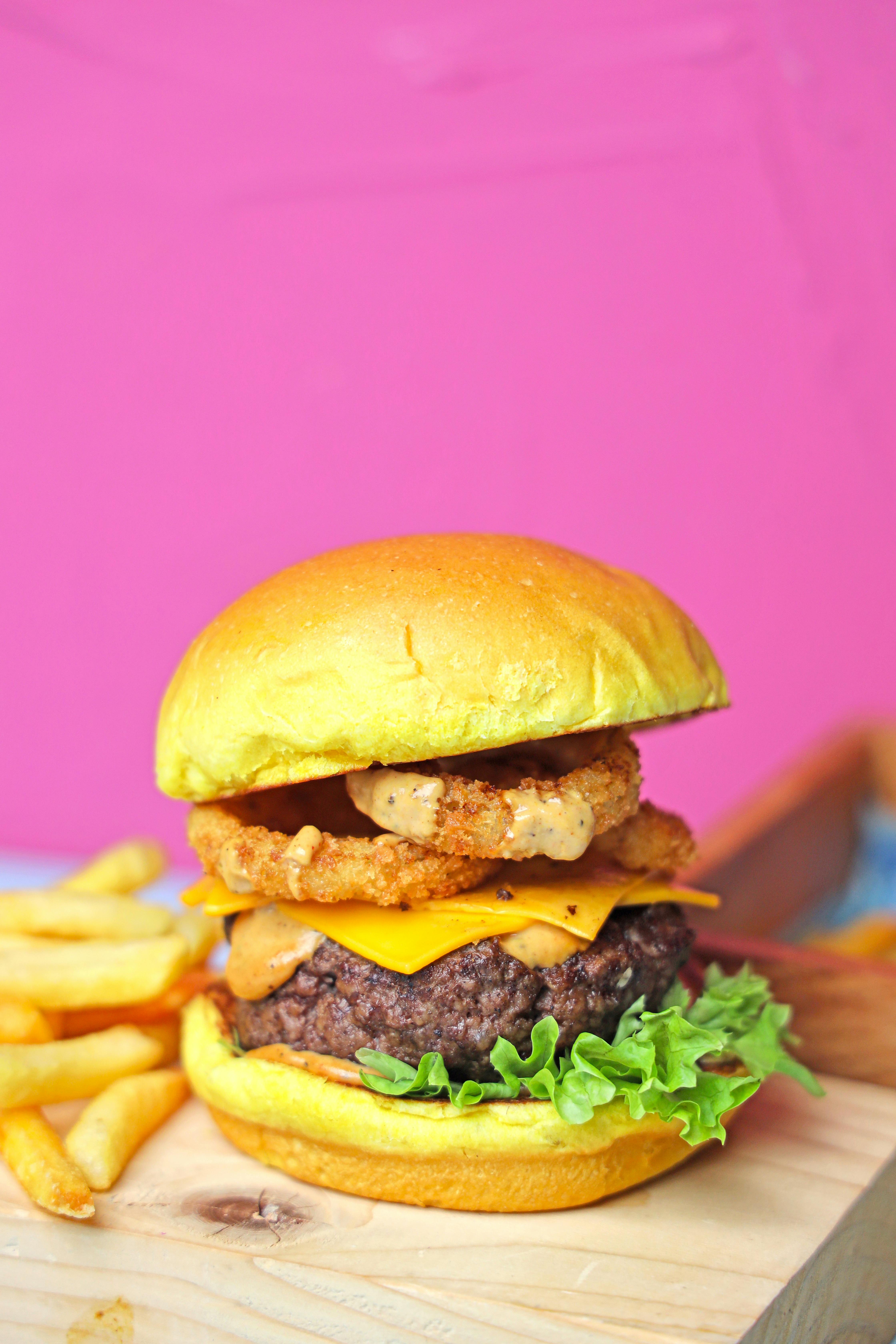 A burger with fried chicken and fries on a wooden cutting board