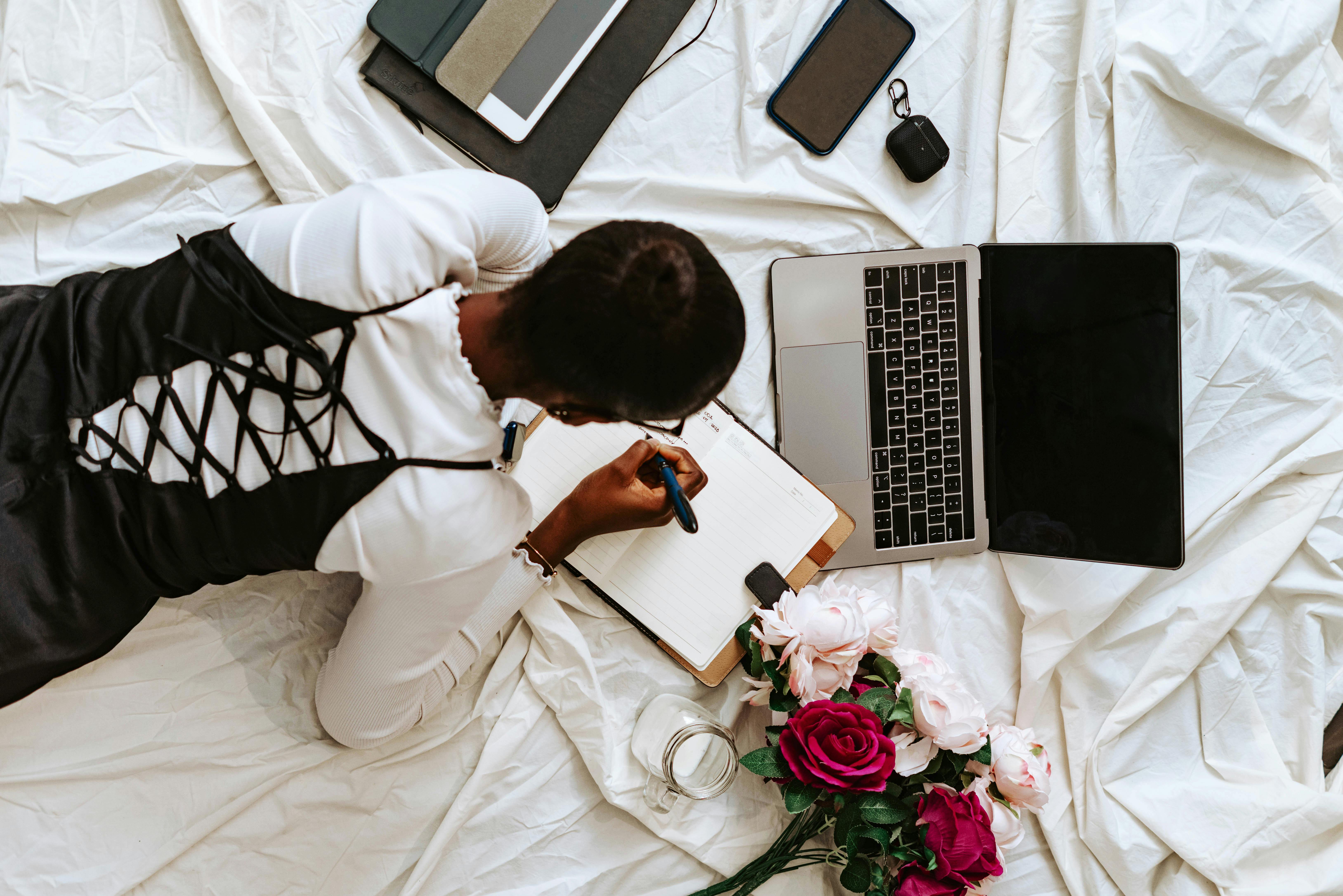 A woman is laying on a bed with a laptop and flowers