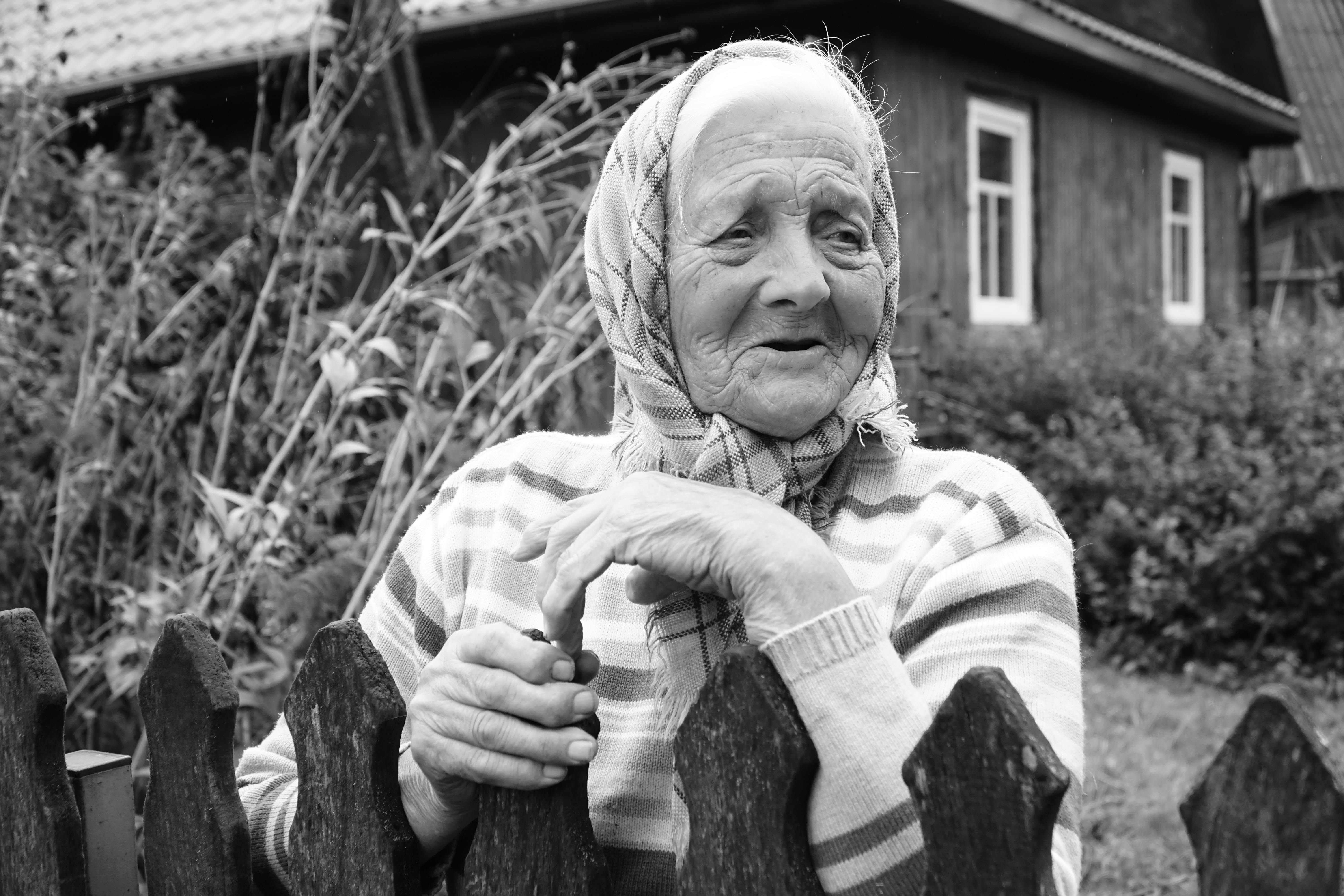 Village Elderly Woman Leaning on the Fence in front of her House