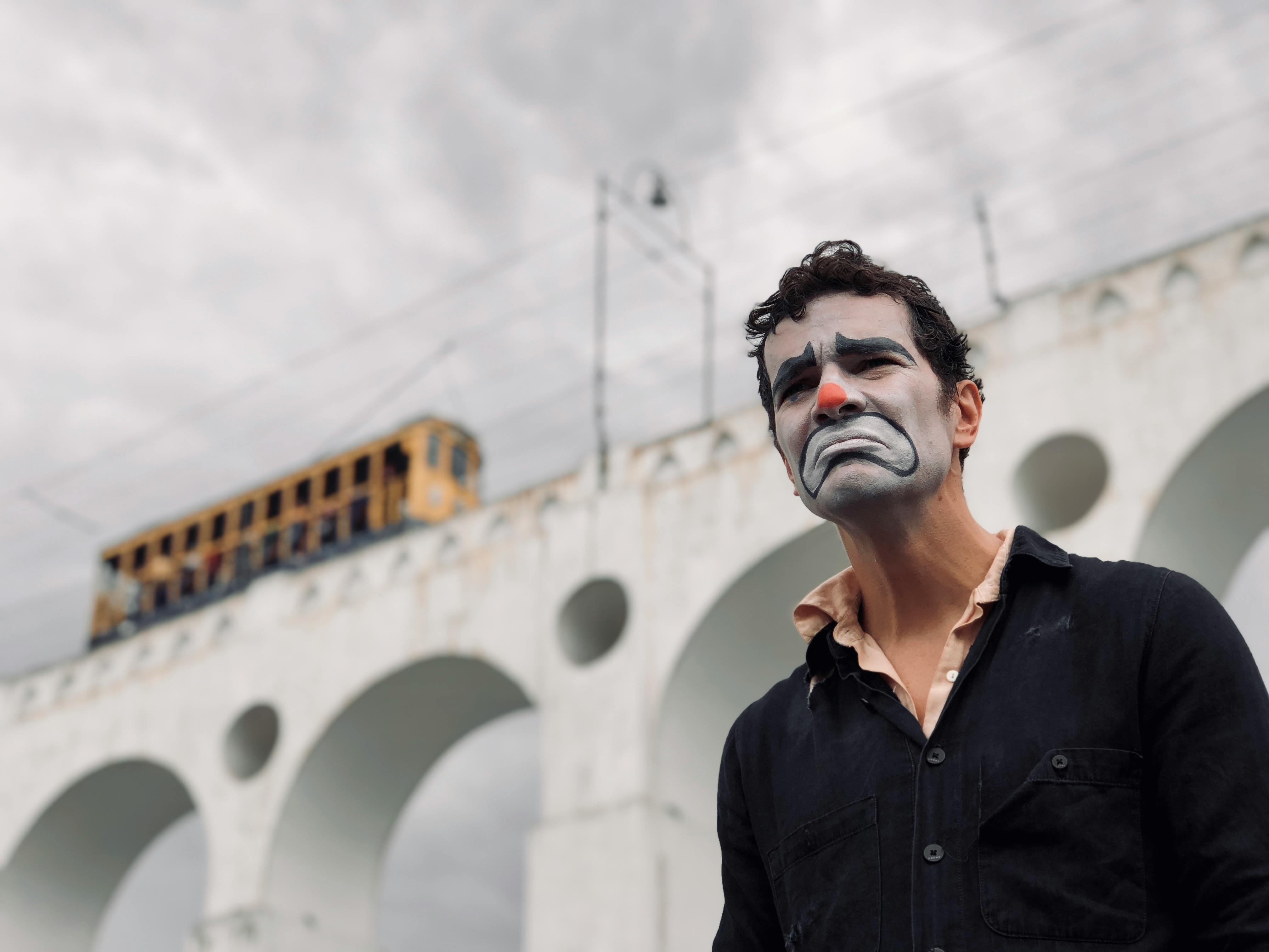 Man Wearing Clown Makeup in Front of a Bridge