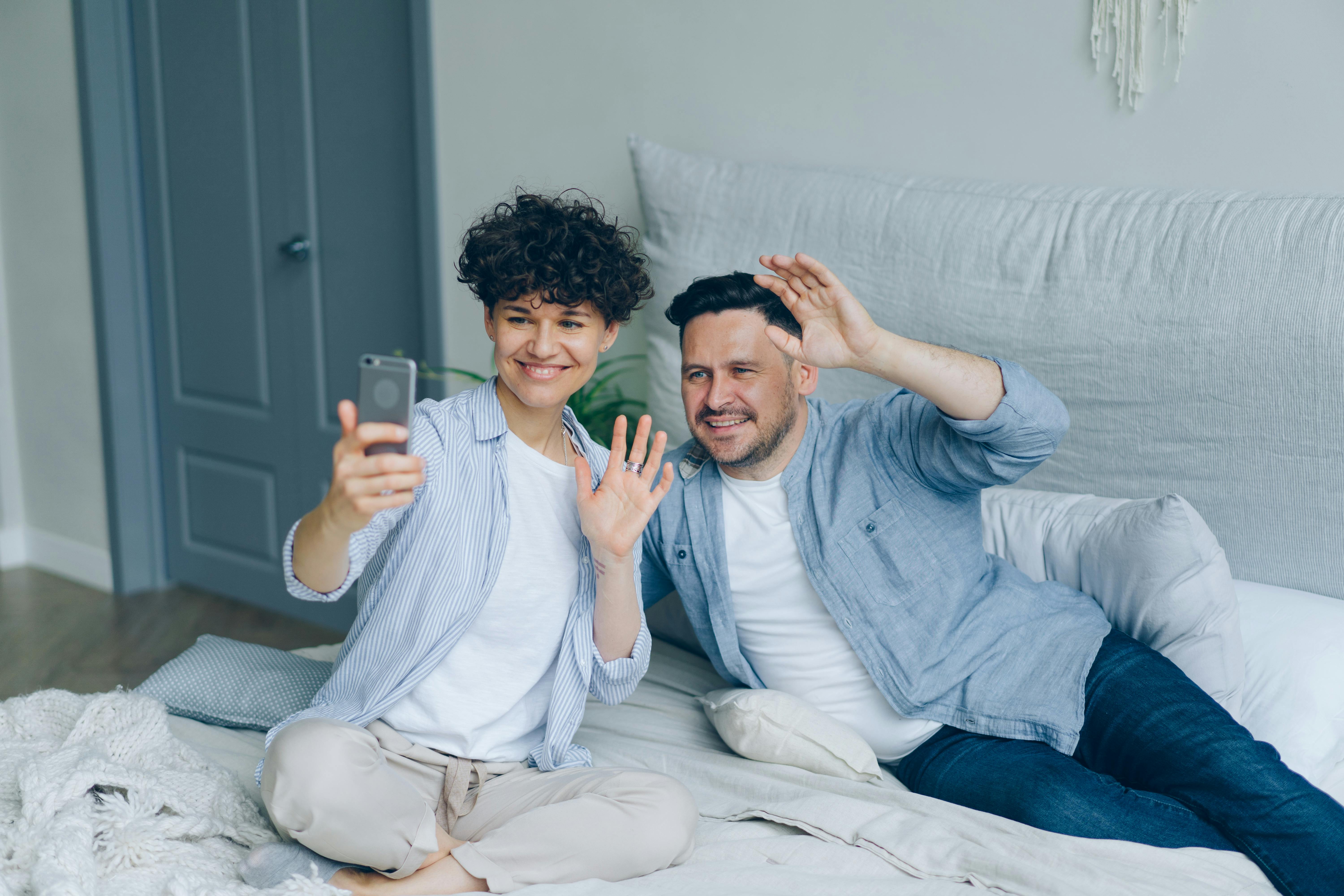 Man and Woman Sitting on a Bed and Taking a Selfie