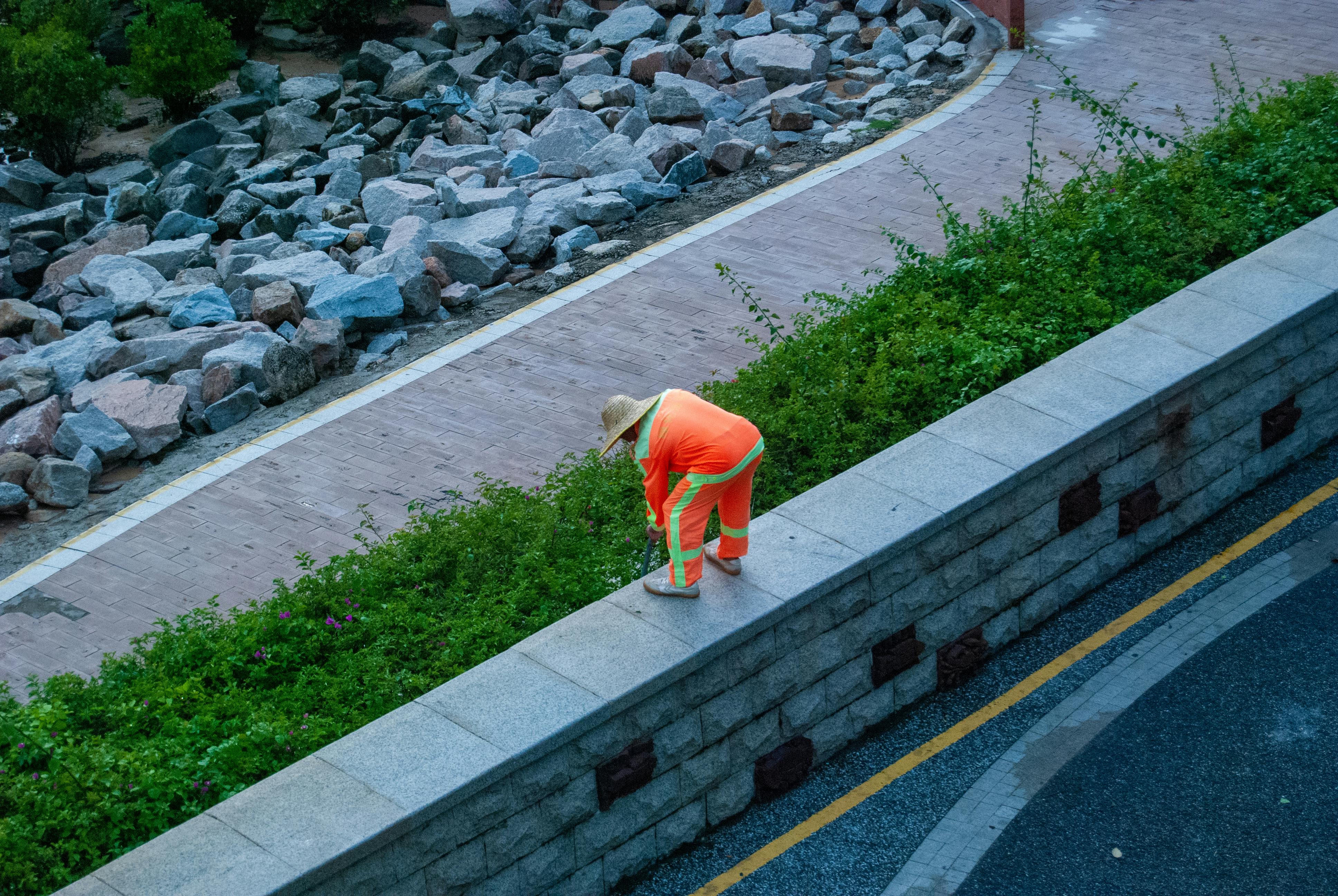 A worker in orange clothing is cleaning the edge of a wall