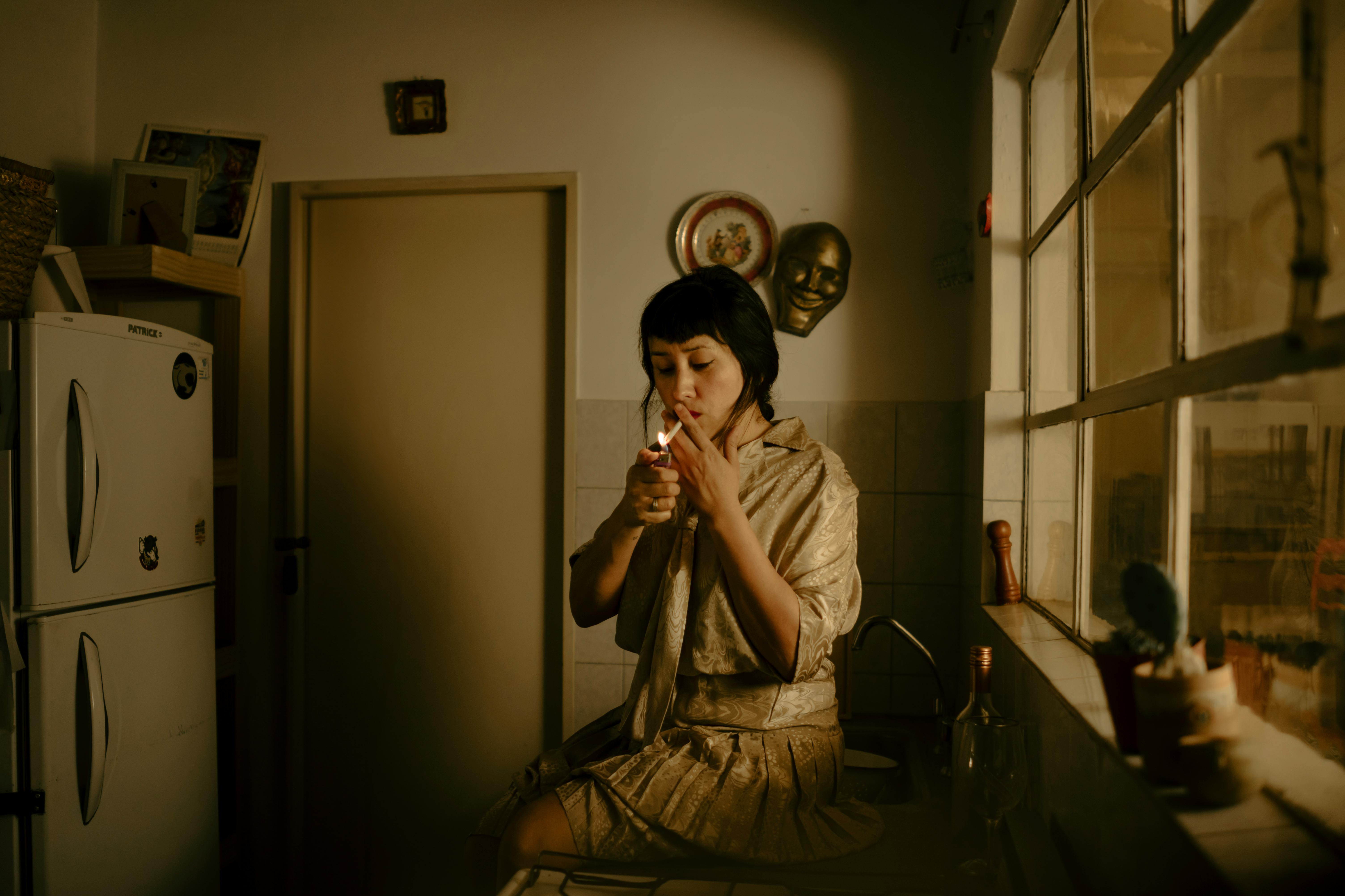 A Woman Sitting in a Kitchen and Smoking a Cigarette