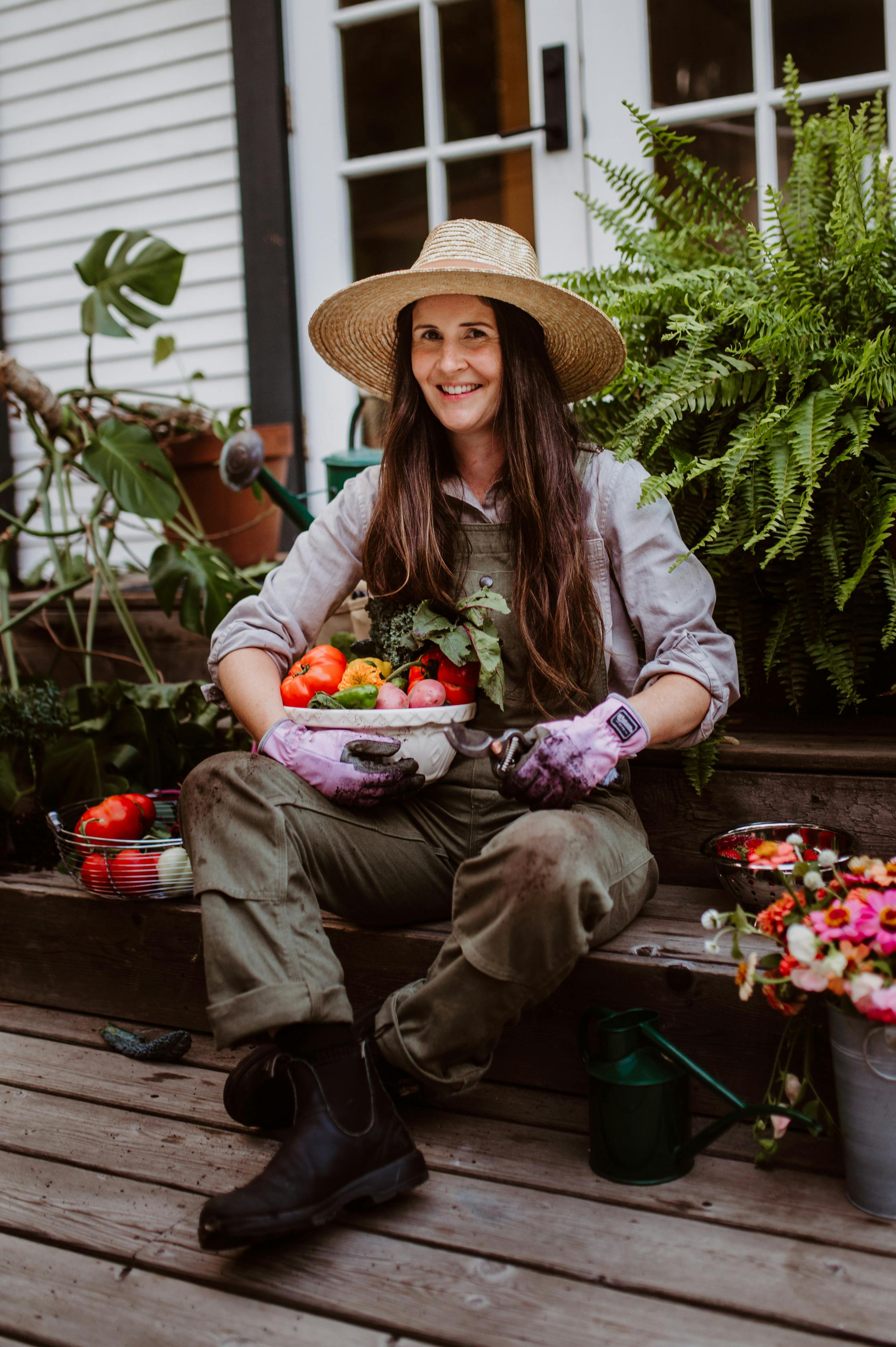 Gardener holding freshly harvested veggies sitting with some of her plants