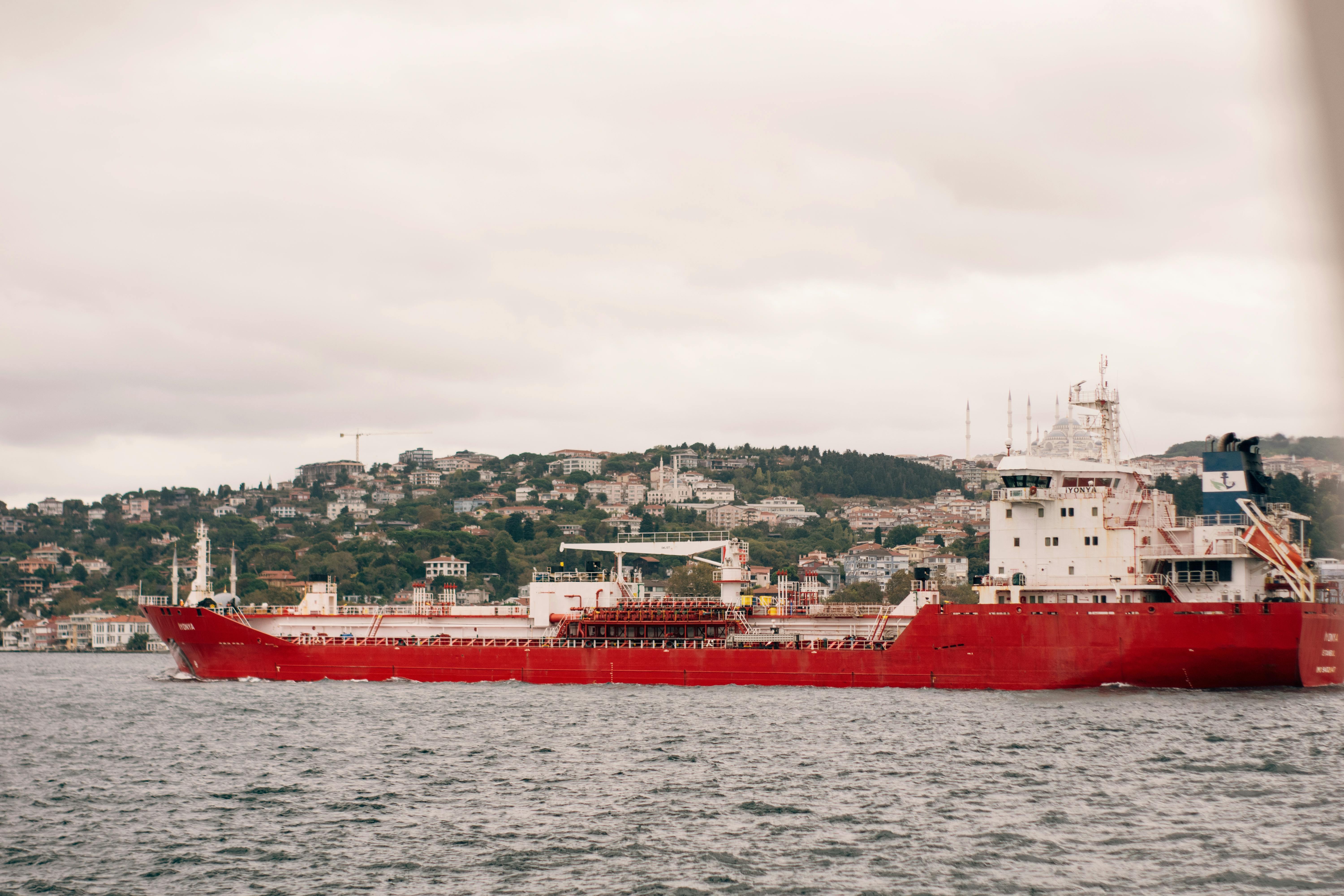 Red Cargo Ship Navigating Near Scenic Coastline