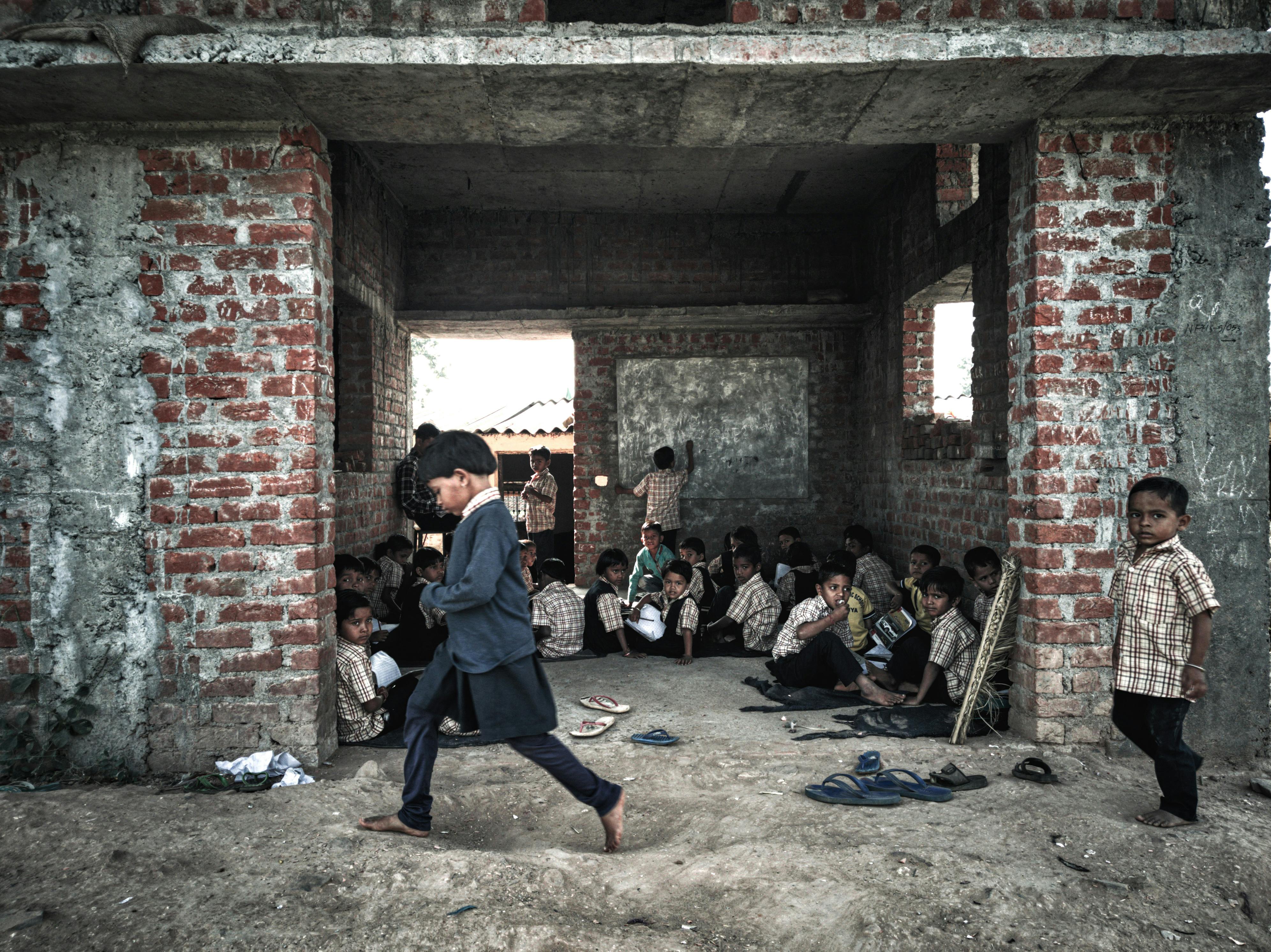 Children Sitting on Floor Inside Building and Another Two Children Walking