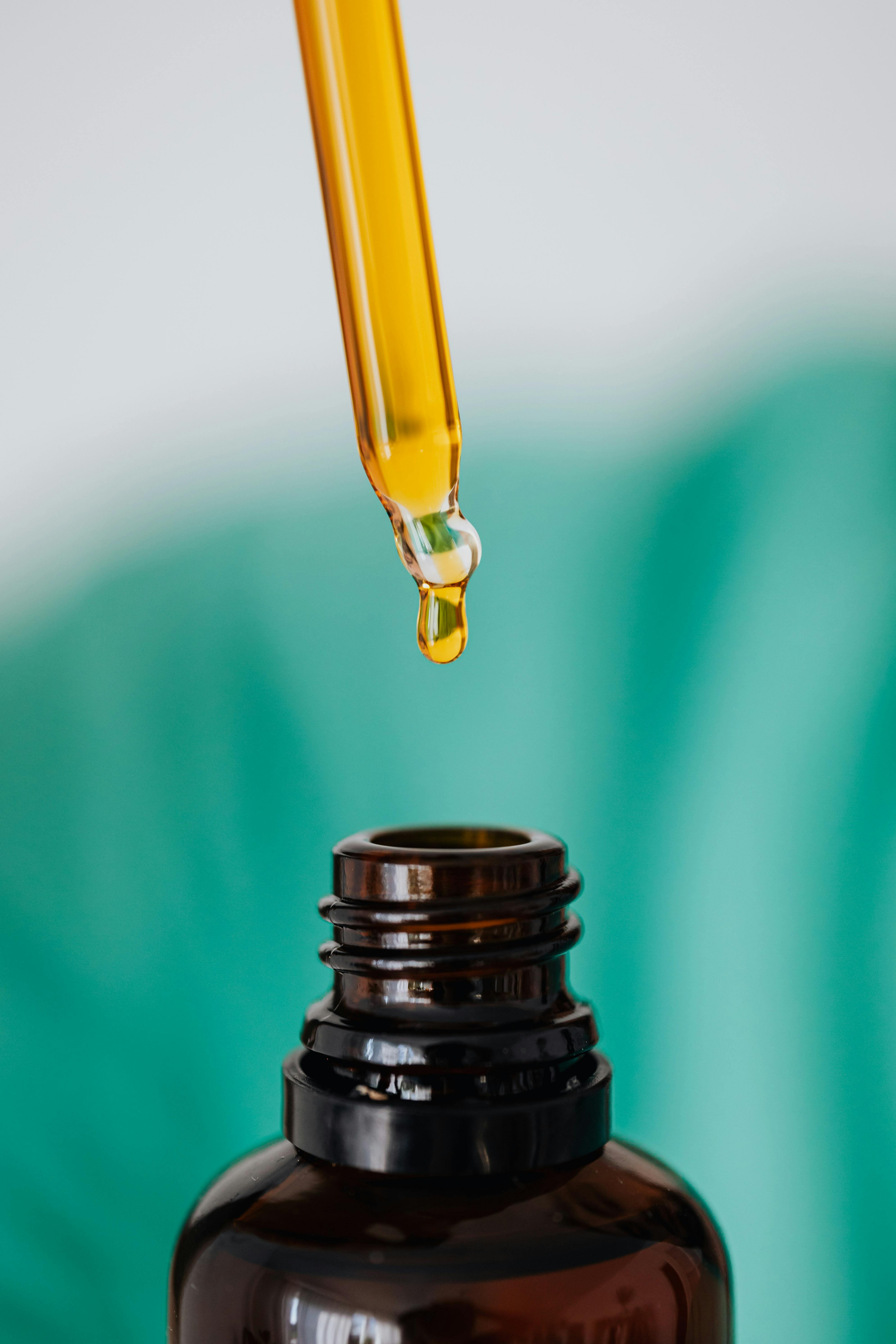 Closeup of anonymous doctor with pipette for fluid dripping yellow medication in brown glass vial while making procedure in clinic