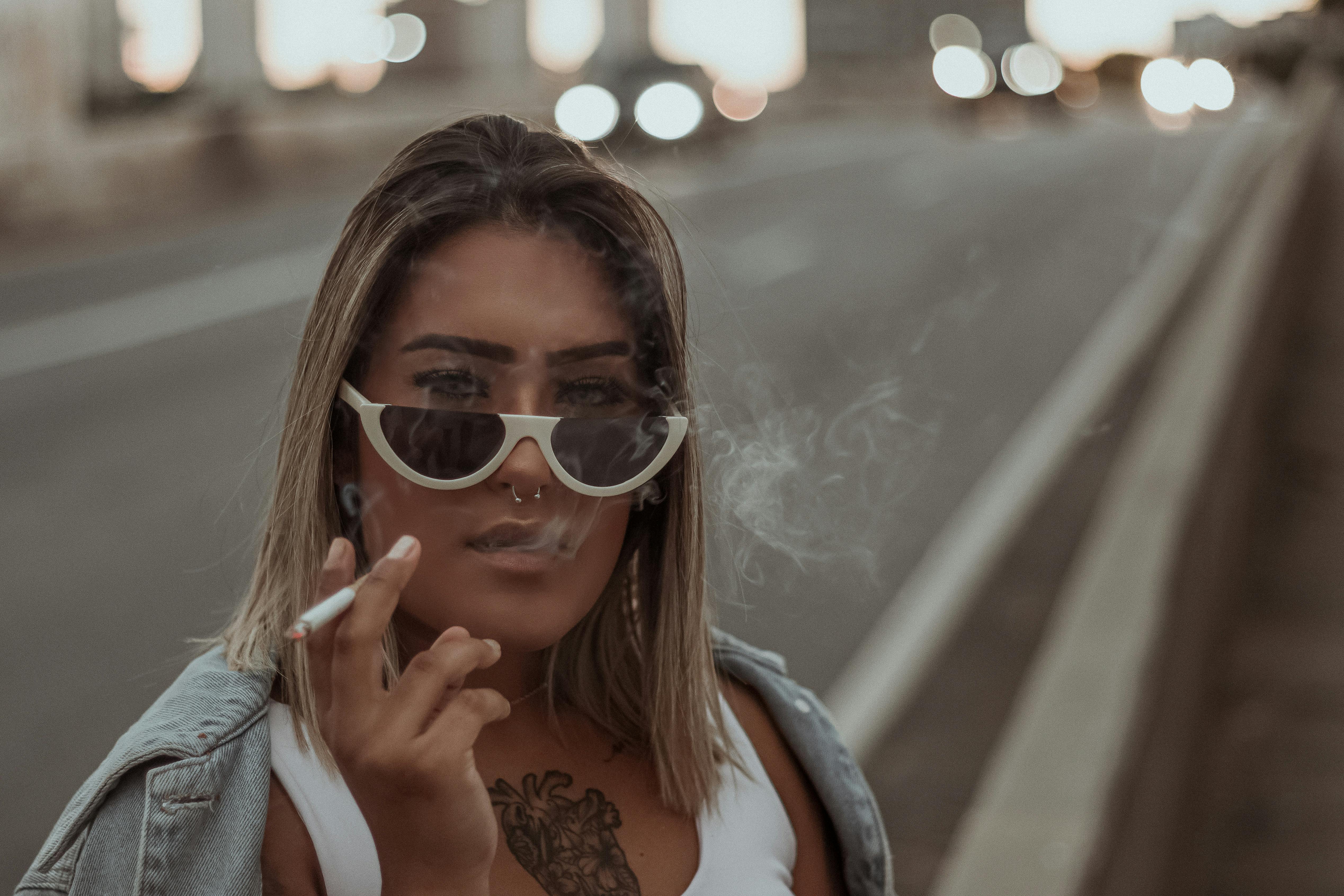 Young beautiful woman in sunglasses smoking on street