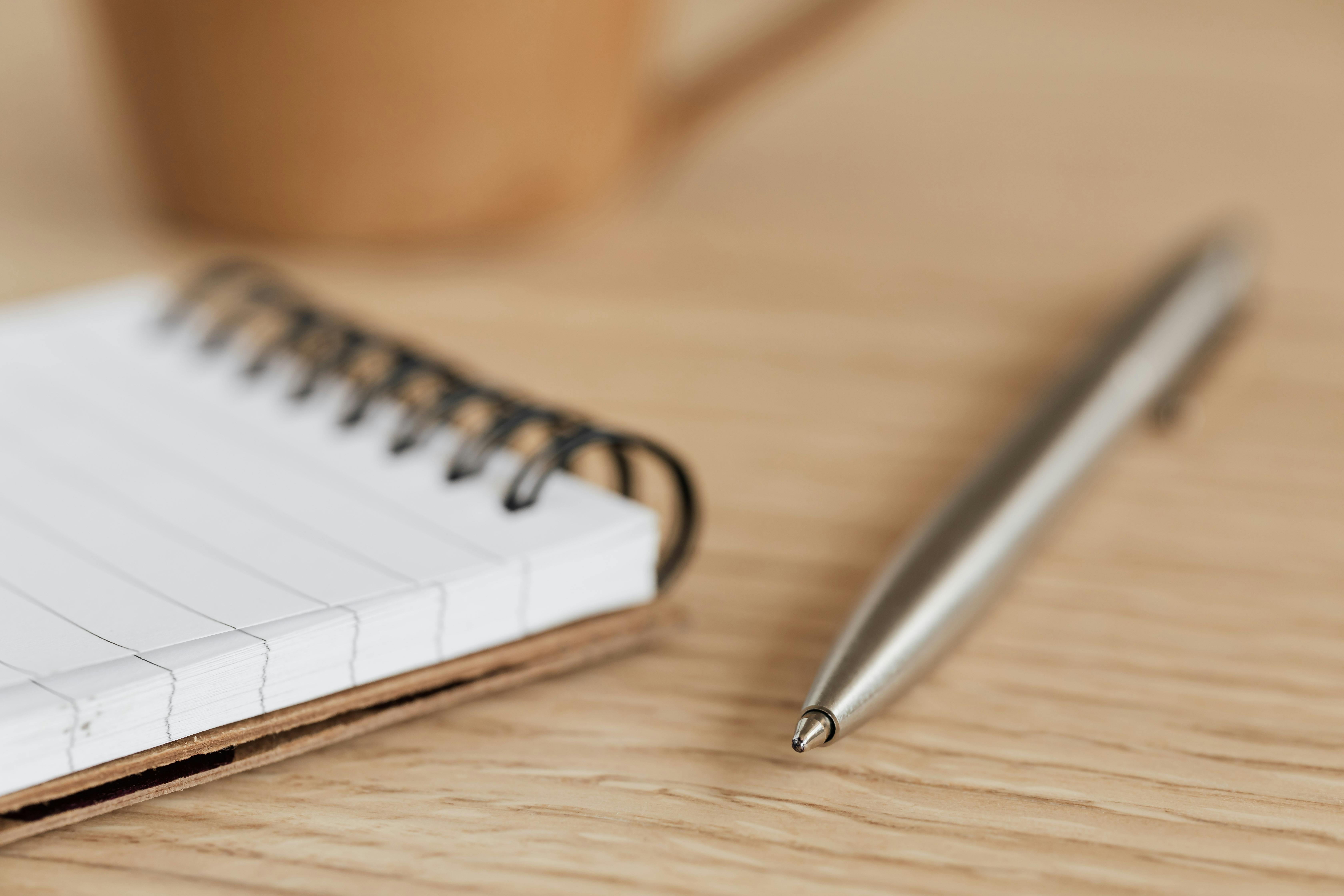 Close Up Photo of Silver Pen Beside a Notepad