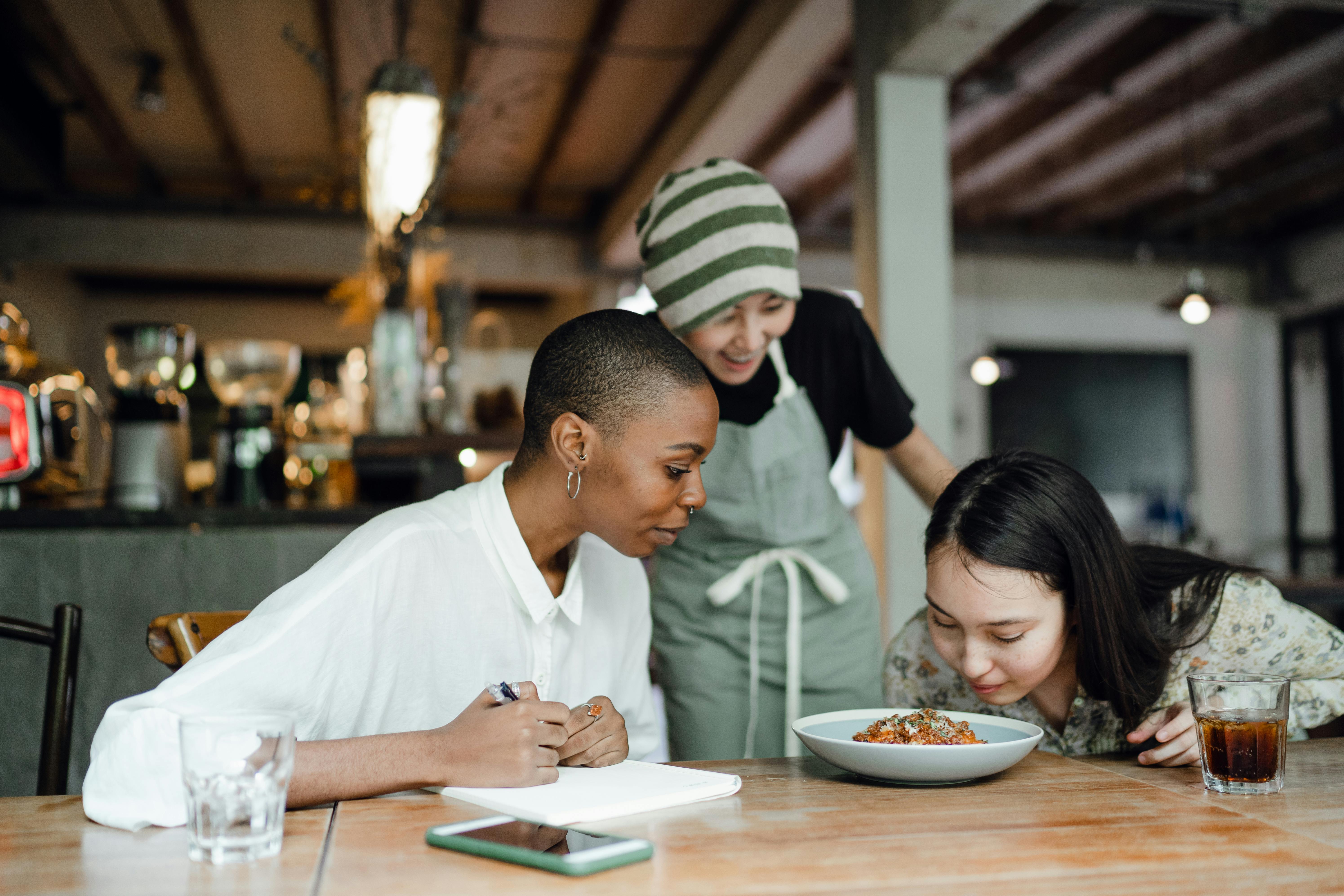 Cheerful coworkers tasting and smelling food in restaurant