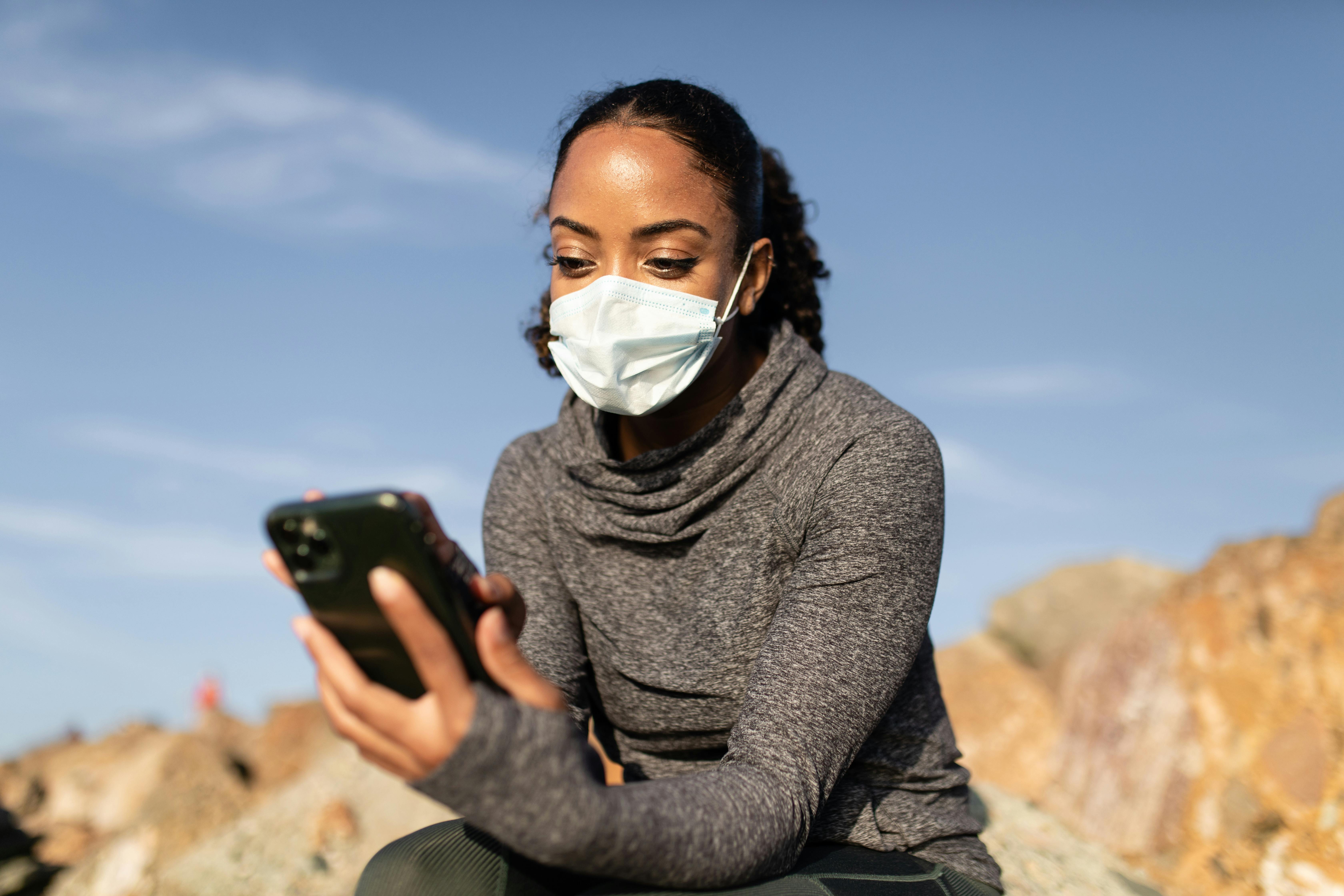 A Woman in a Face Mask Using her Smartphone