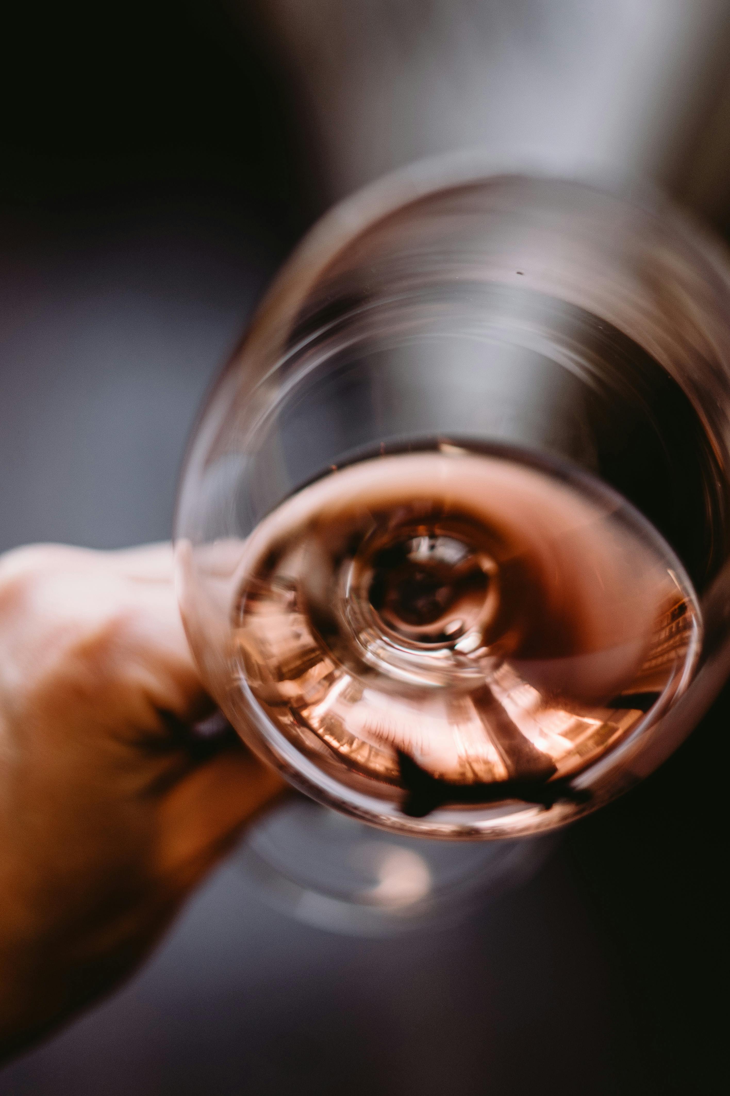 From above crop person holding wineglass with aged flavorful rose wine against blurred background