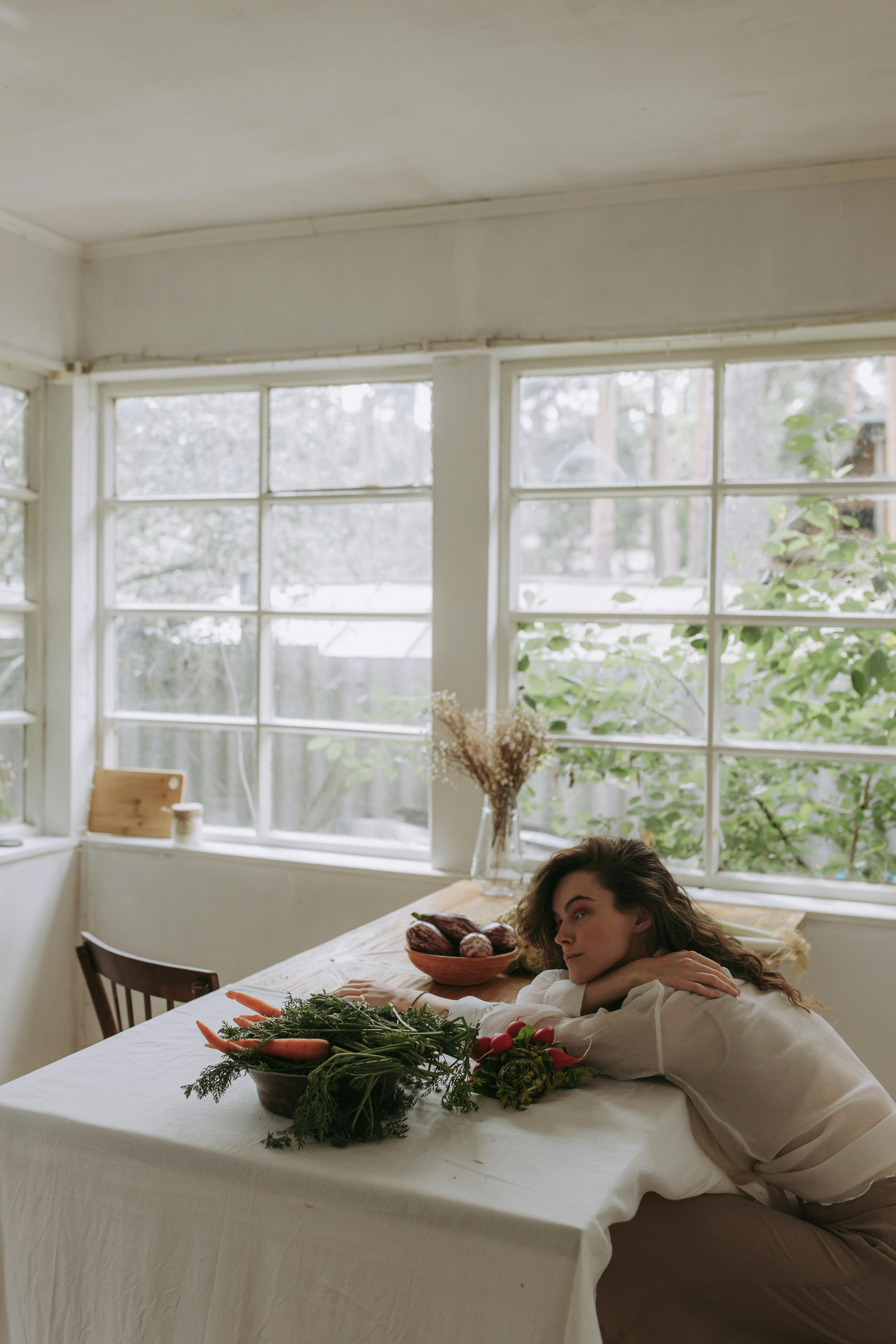 Woman in White Long Sleeve Shirt Sitting Behind A Table With Vegetables