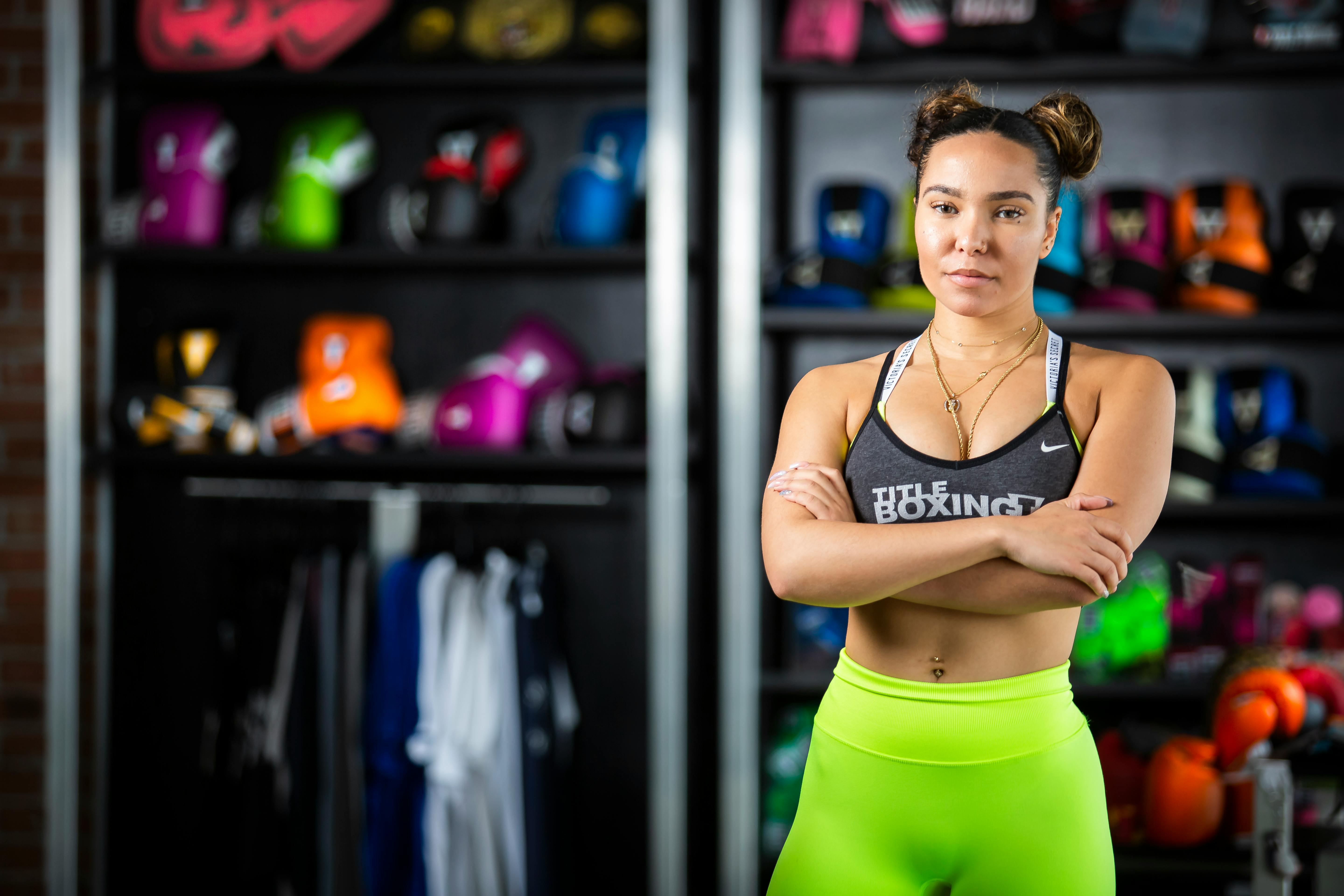 A Woman in Activewear Standing Near Wooden Shelves with Boxing Gloves