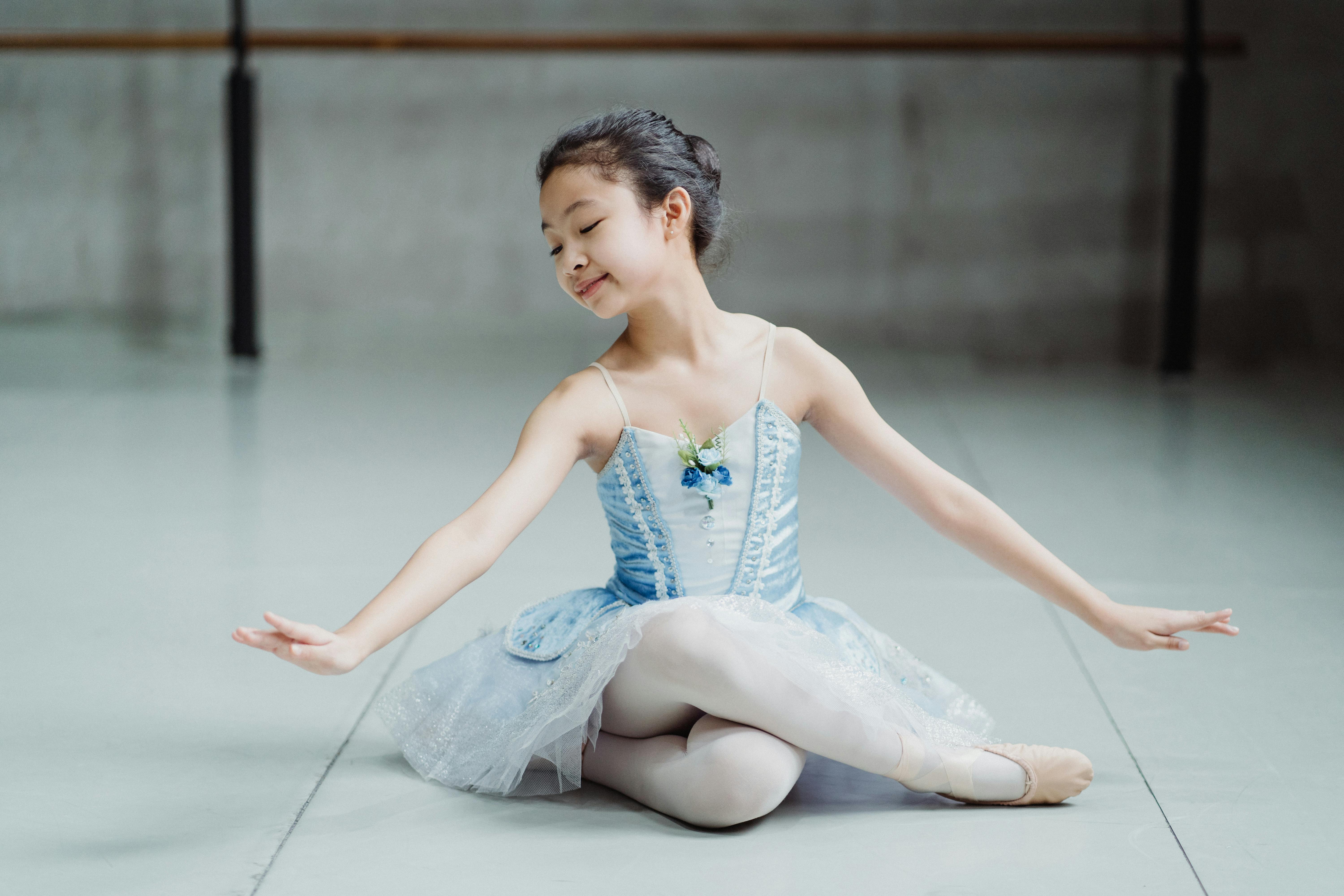 Little ethnic charming ballerina sitting on floor in ballet studio
