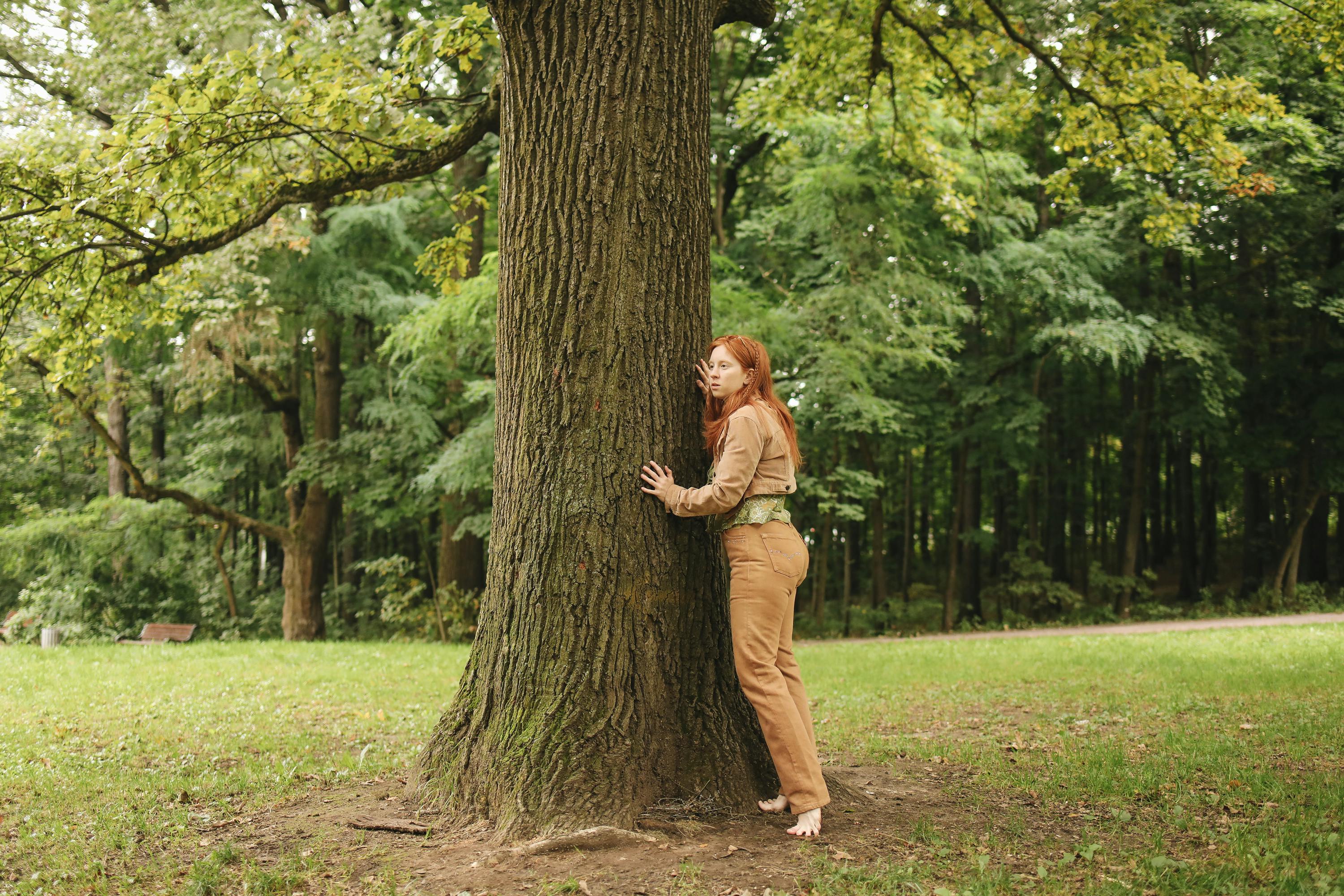 A Woman in Brown Pants and Jacket Standing Barefooted Beside the Tree