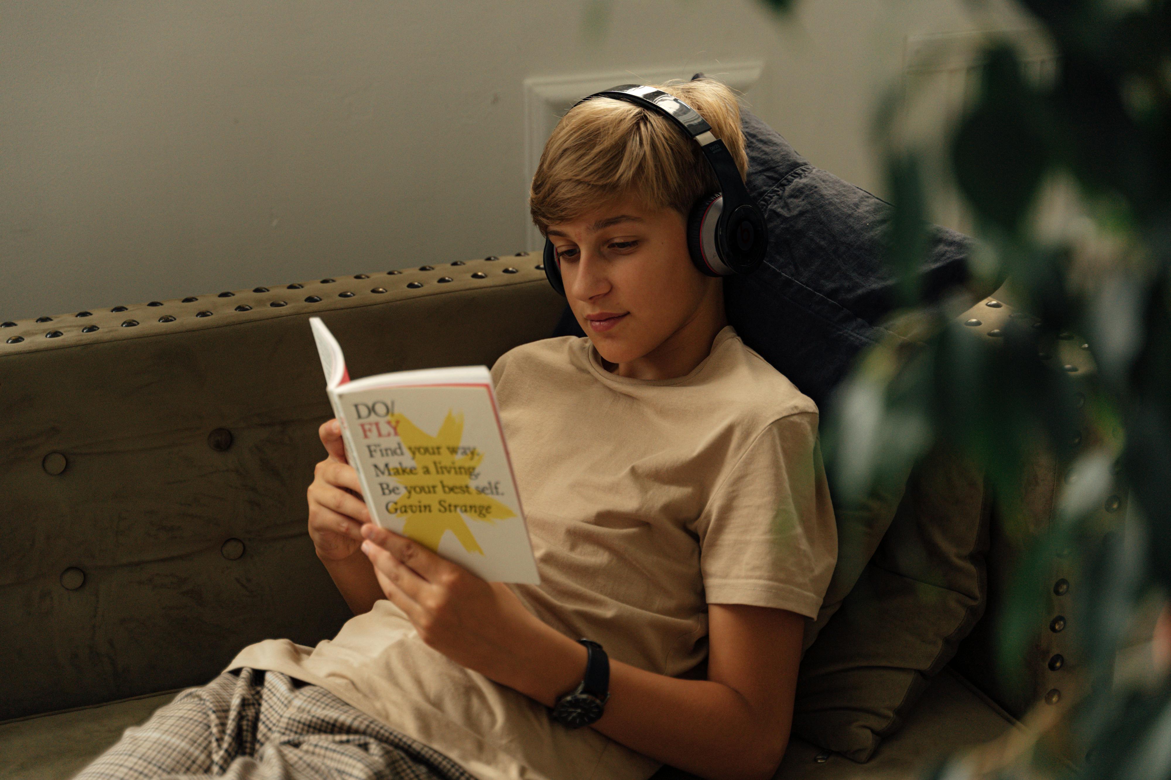 A Boy Reading a Book while Listening to Music