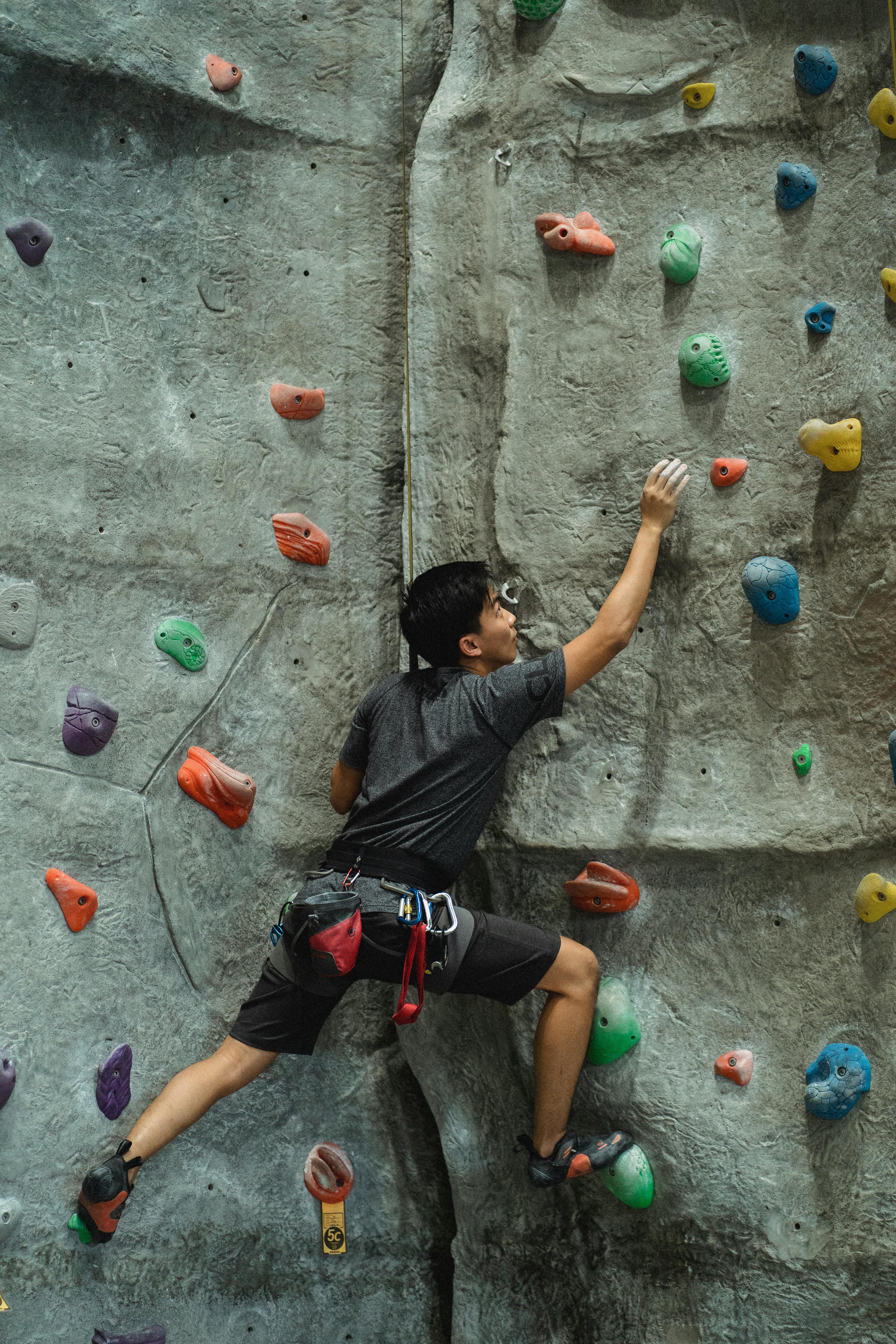 Concentrated male mountaineer in sportswear training on climbing wall in modern bouldering center