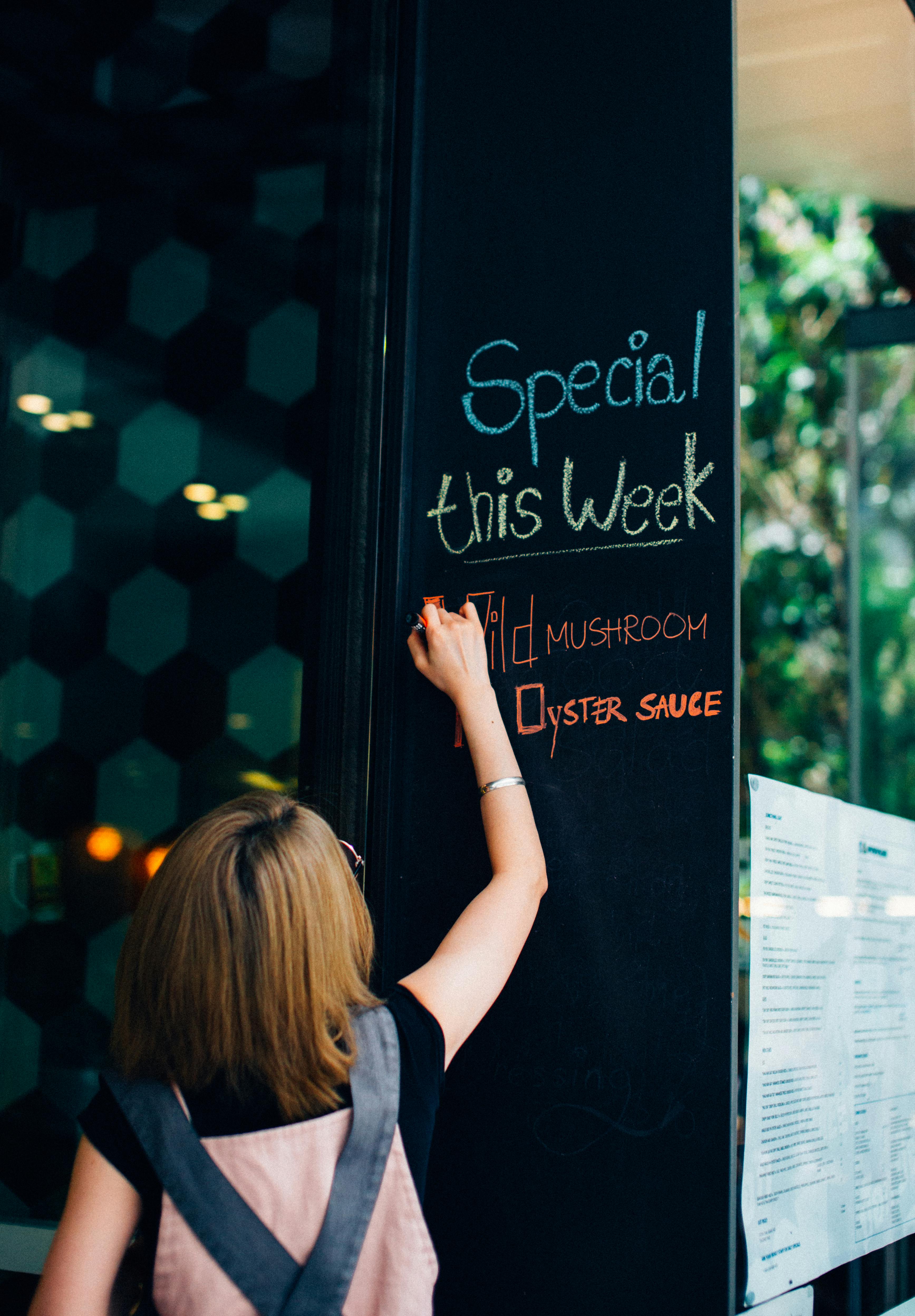Woman Writing with Chalk on Board in Restaurant 