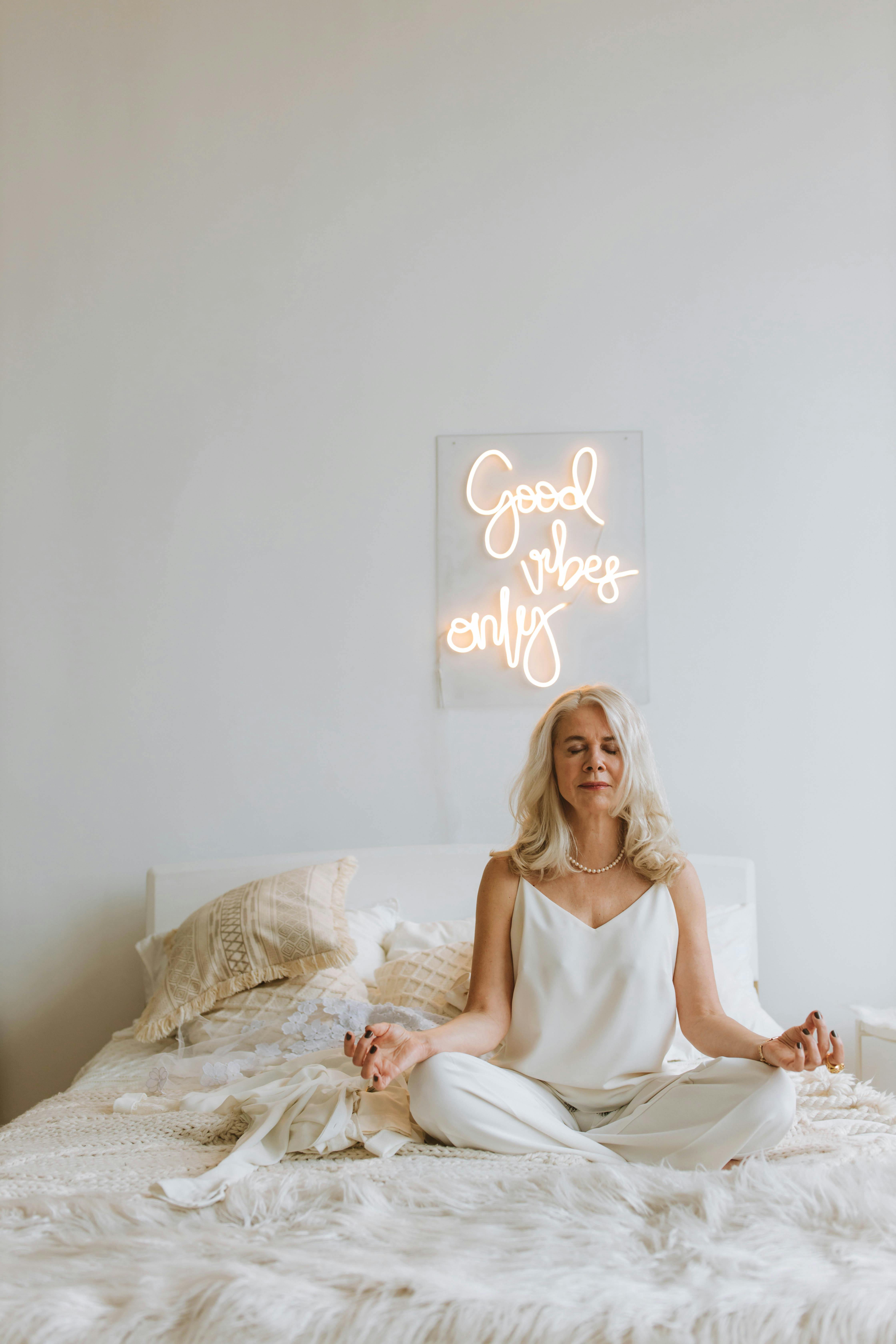 Woman in White Strap Top Sitting on Bed in Lotus Pose with Eyes Closed