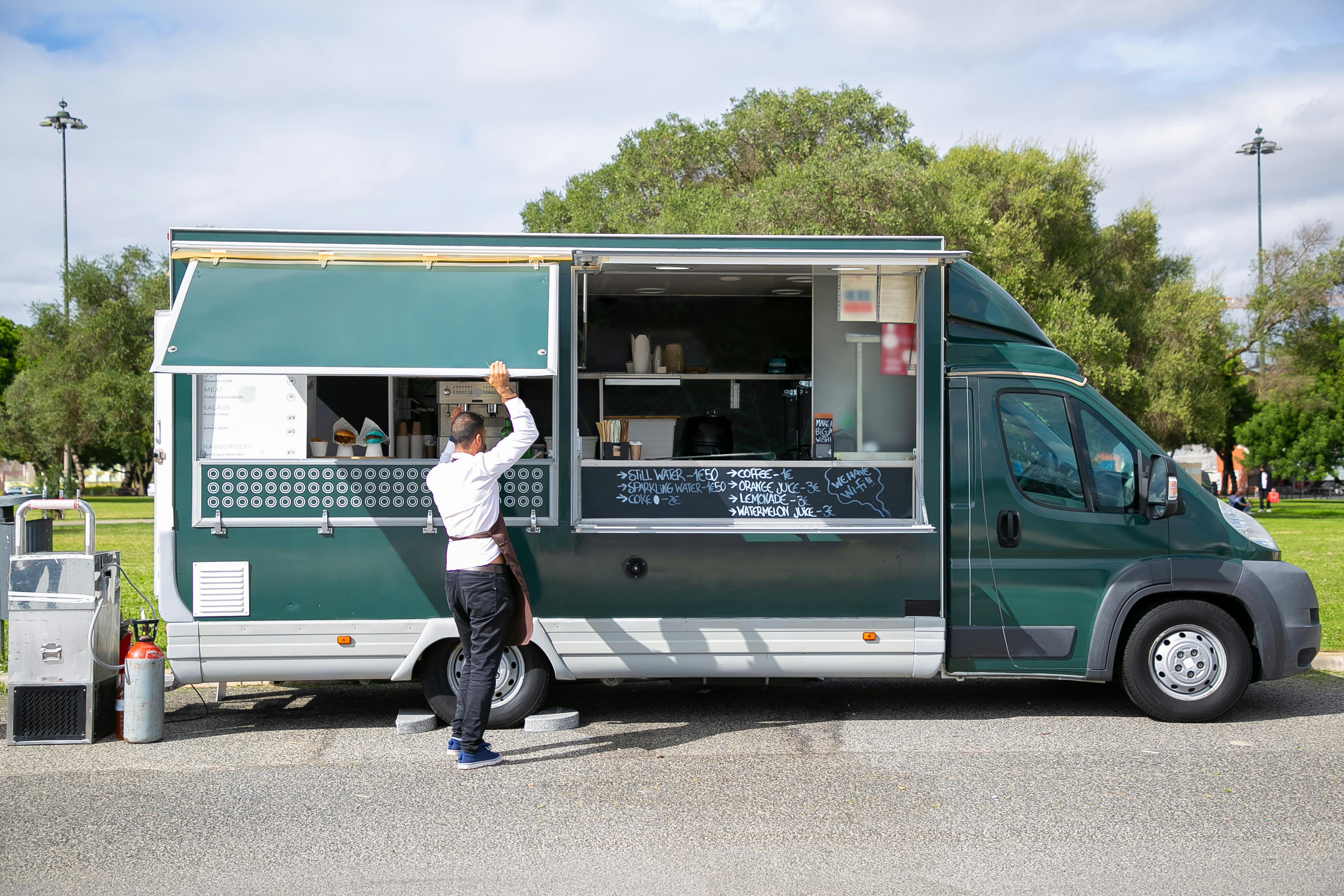 Back view full body of anonymous male worker opening windows of car with street food parked in park