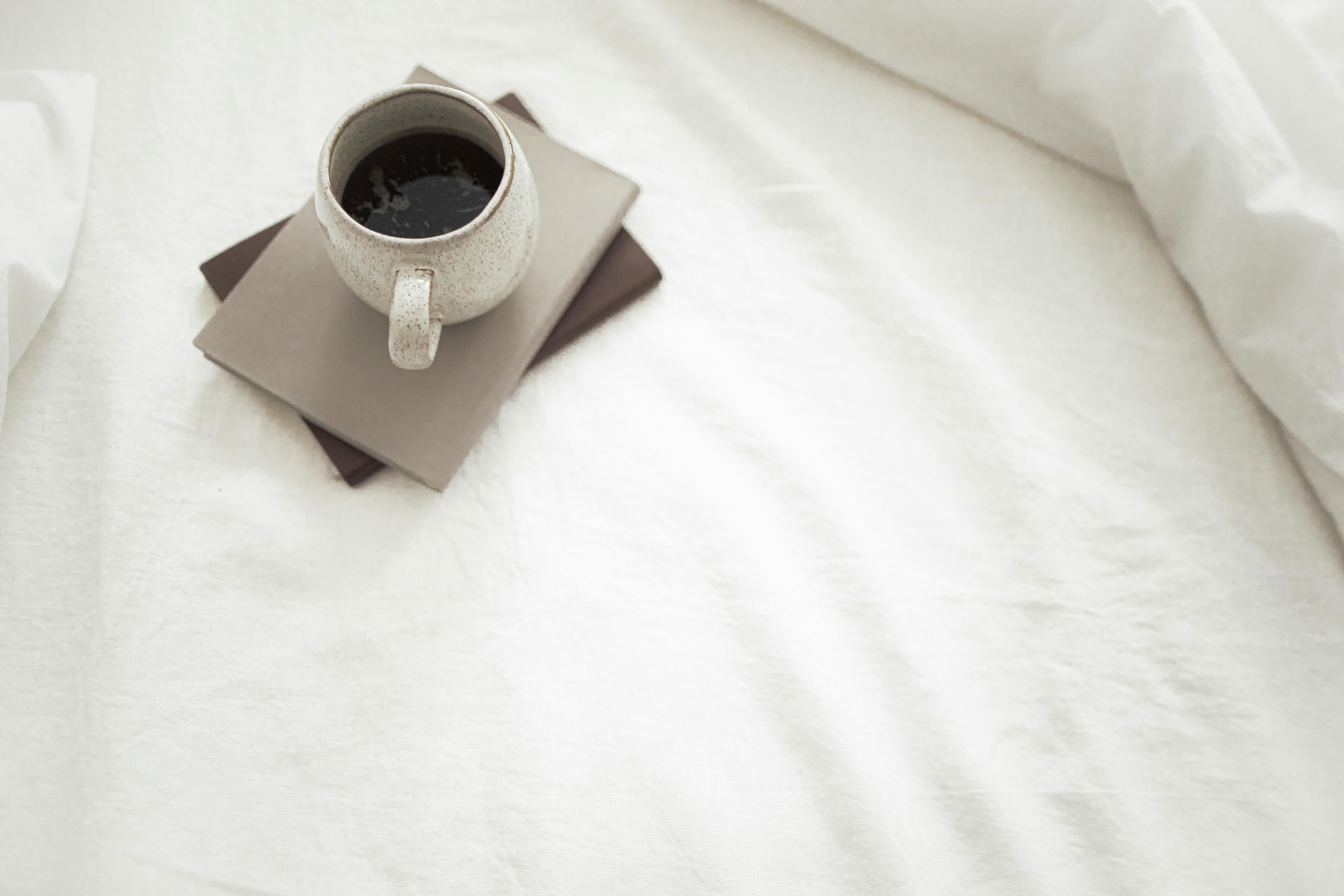 Cup of aromatic coffee and notebooks placed on white bed