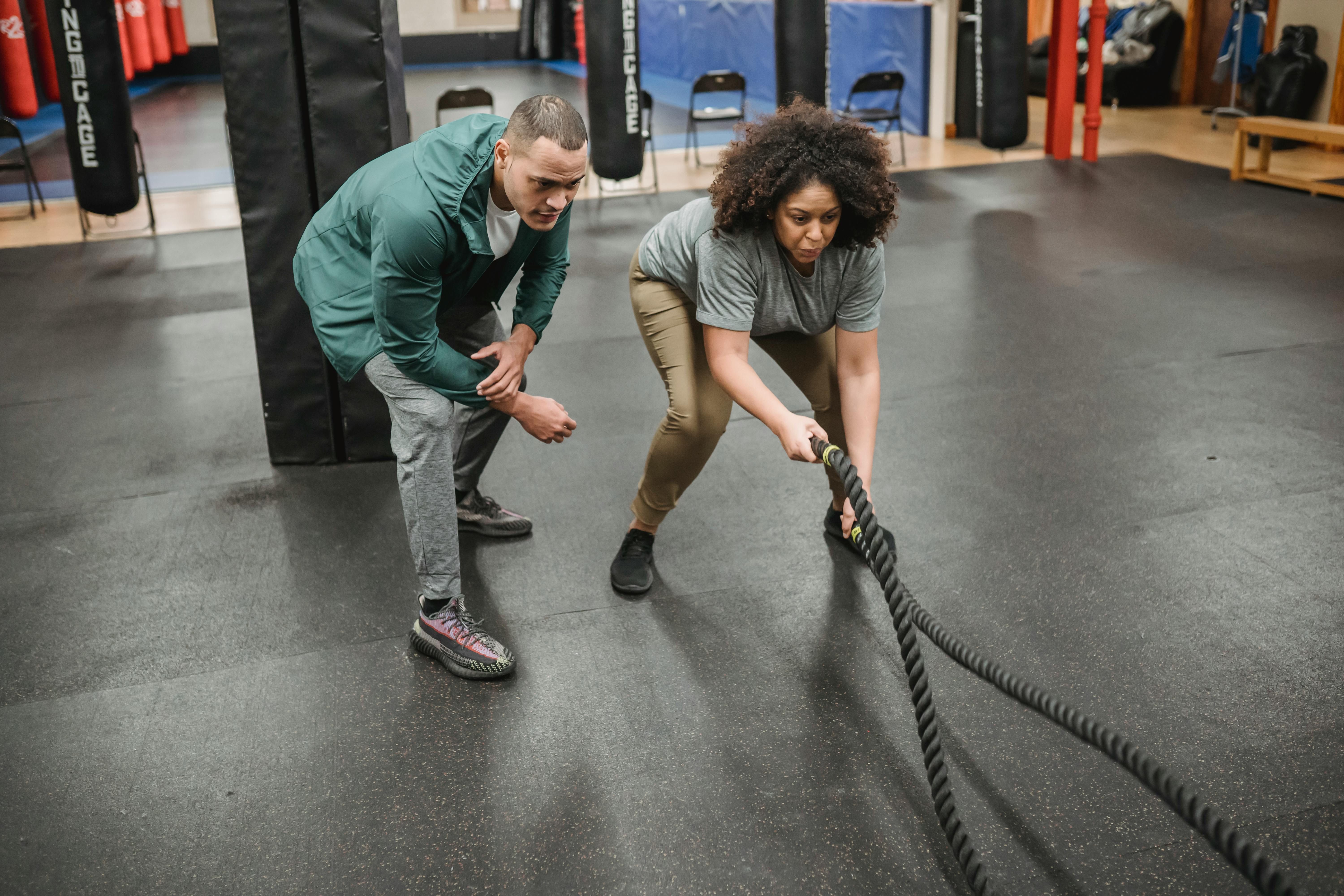 Strong coach training black woman exercising with battle ropes