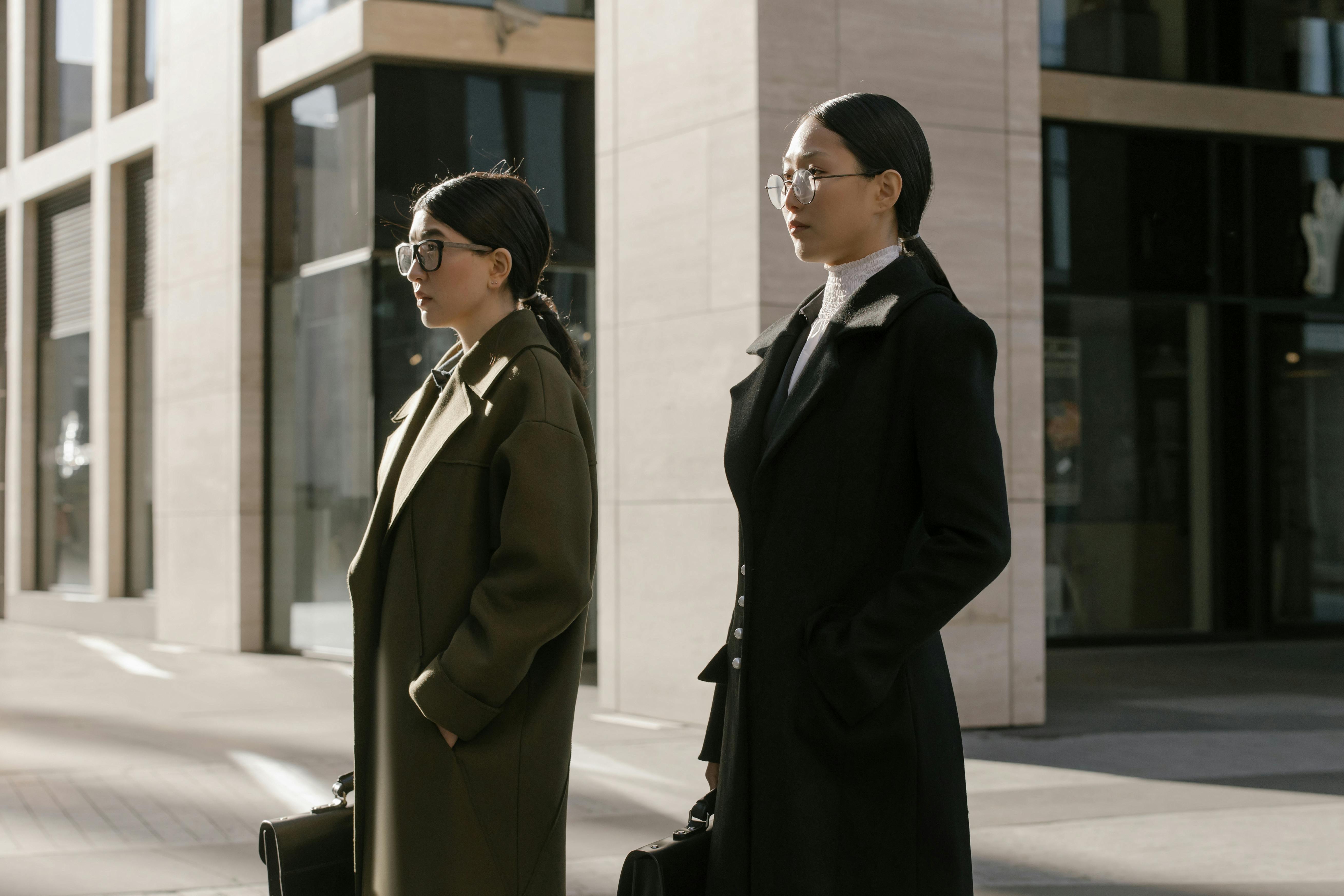 Woman in Coats Standing Together Near a White Building