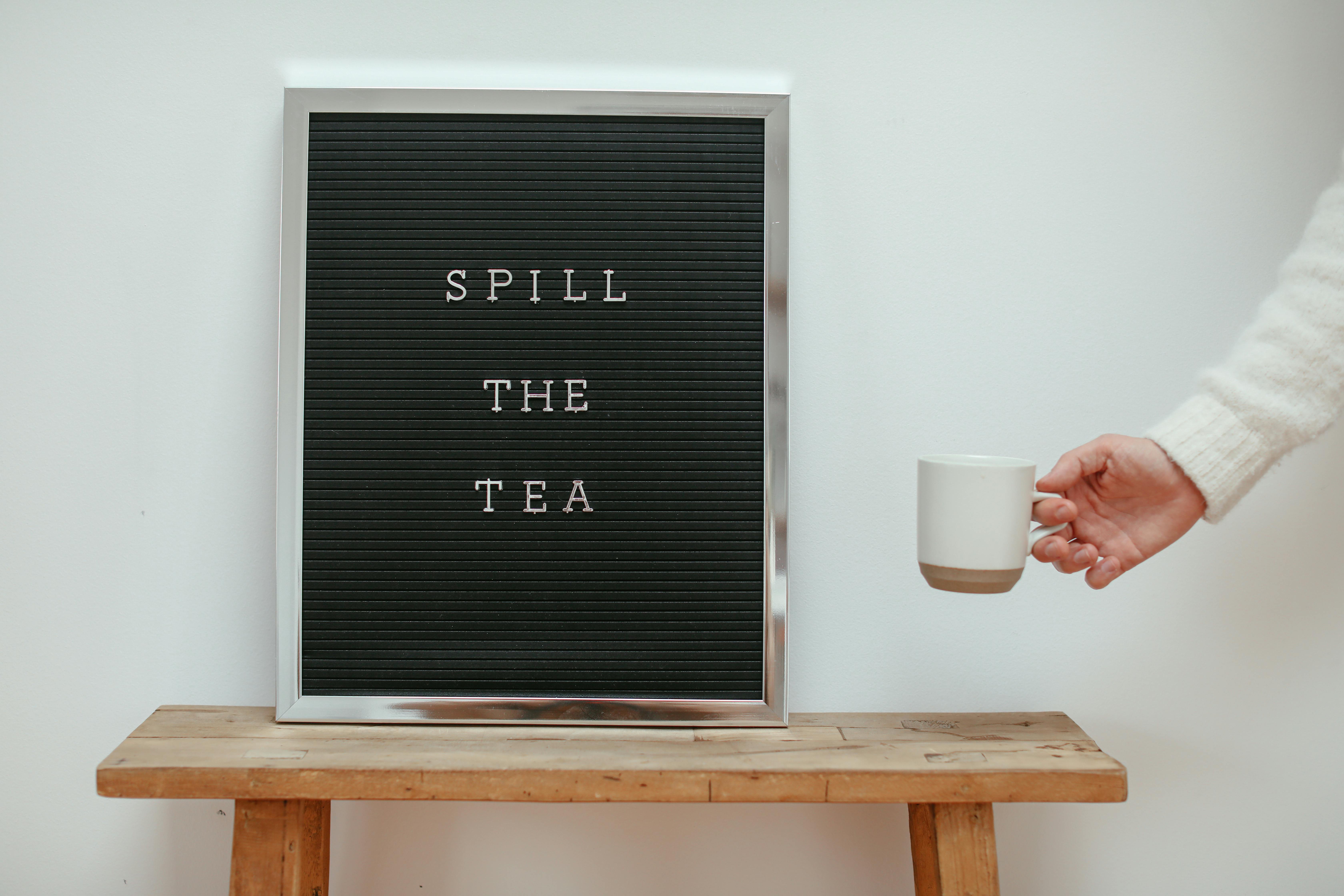 A Hand Holding a Mug Near the Wooden Table with Letter Board